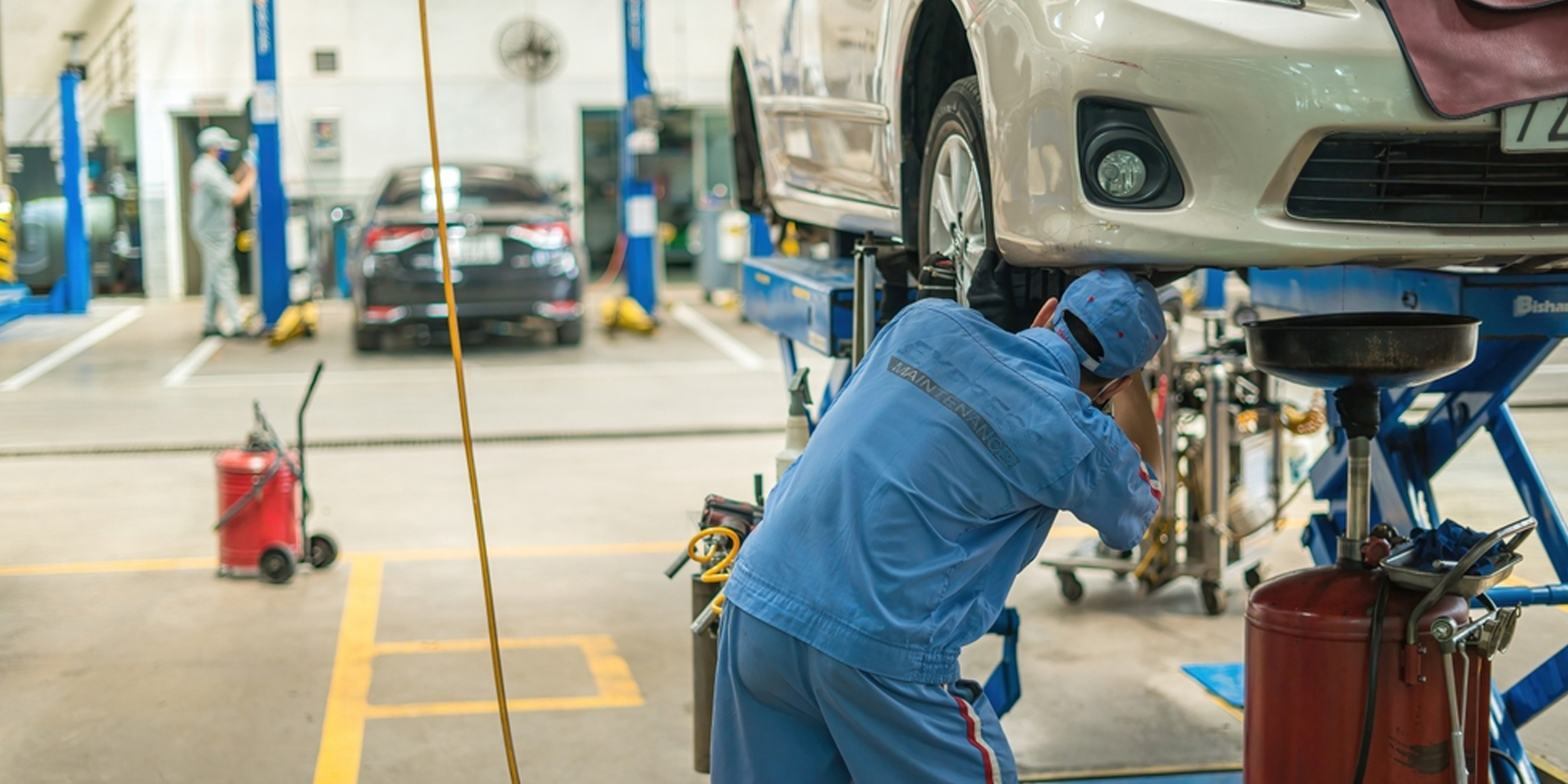 Ein Mechaniker arbeitet unter einem angehobenen Auto in einer geschäftigen Autowerkstatt | Quelle: Shutterstock