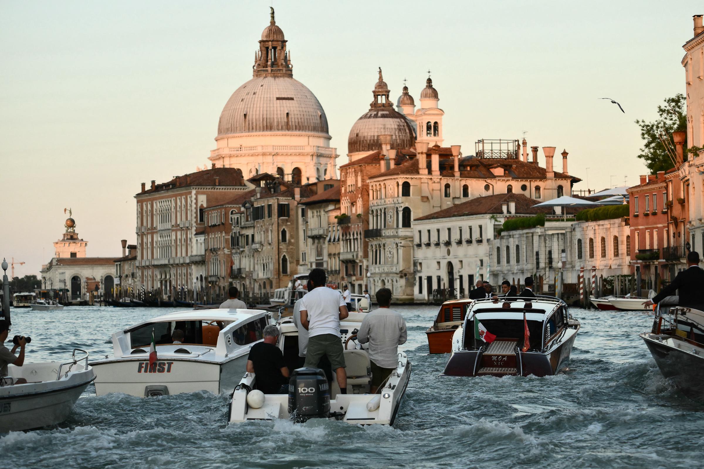 Motorboote schlängeln sich den Kanal entlang, während das goldene Licht die großen Kuppeln und historischen Fassaden Venedigs beleuchtet und die lebhafte Szene hinter dem Wassertaxi von Jeff Bezos und Lauren Sánchez einfängt.