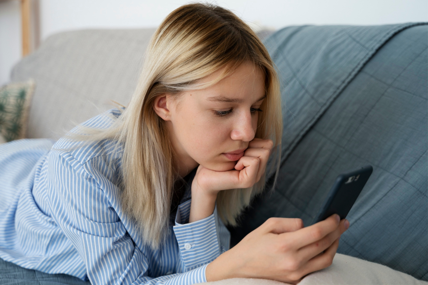 Ein trauriges Teenager-Mädchen, das auf der Couch liegt und auf ihr Telefon schaut | Quelle: Freepik