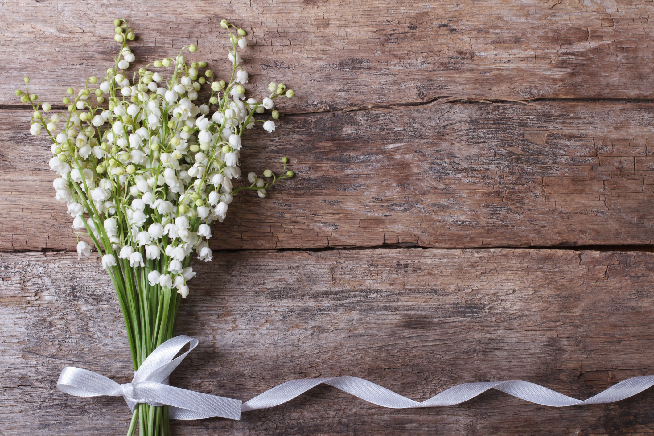 Schöner Blumenrahmen mit Maiglöckchenblumen auf altem Holztisch I Quelle: Getty Images