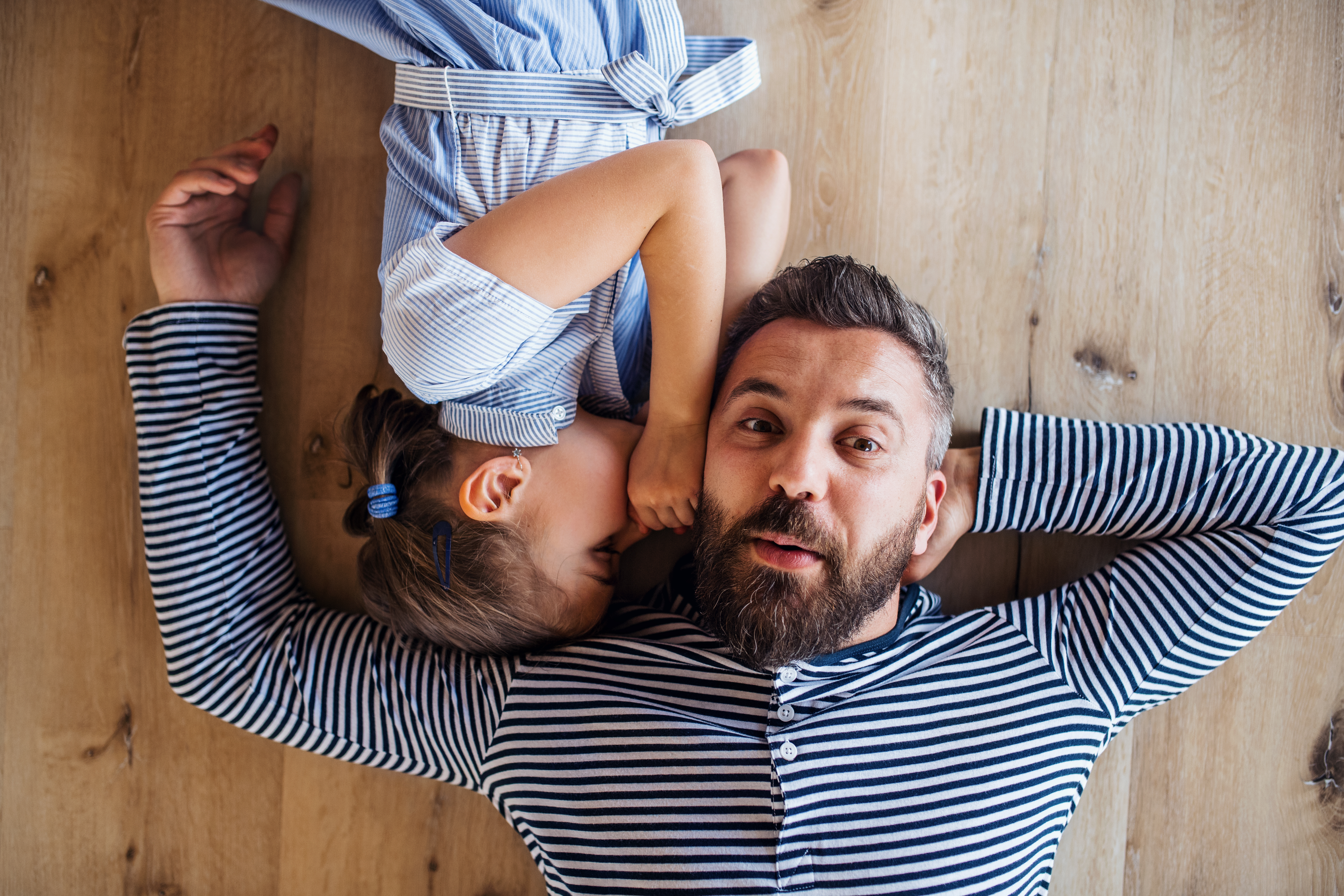 Draufsicht auf einen reifen Vater und seine kleine Tochter, die zu Hause auf dem Boden liegen und flüstern | Quelle: Getty Images