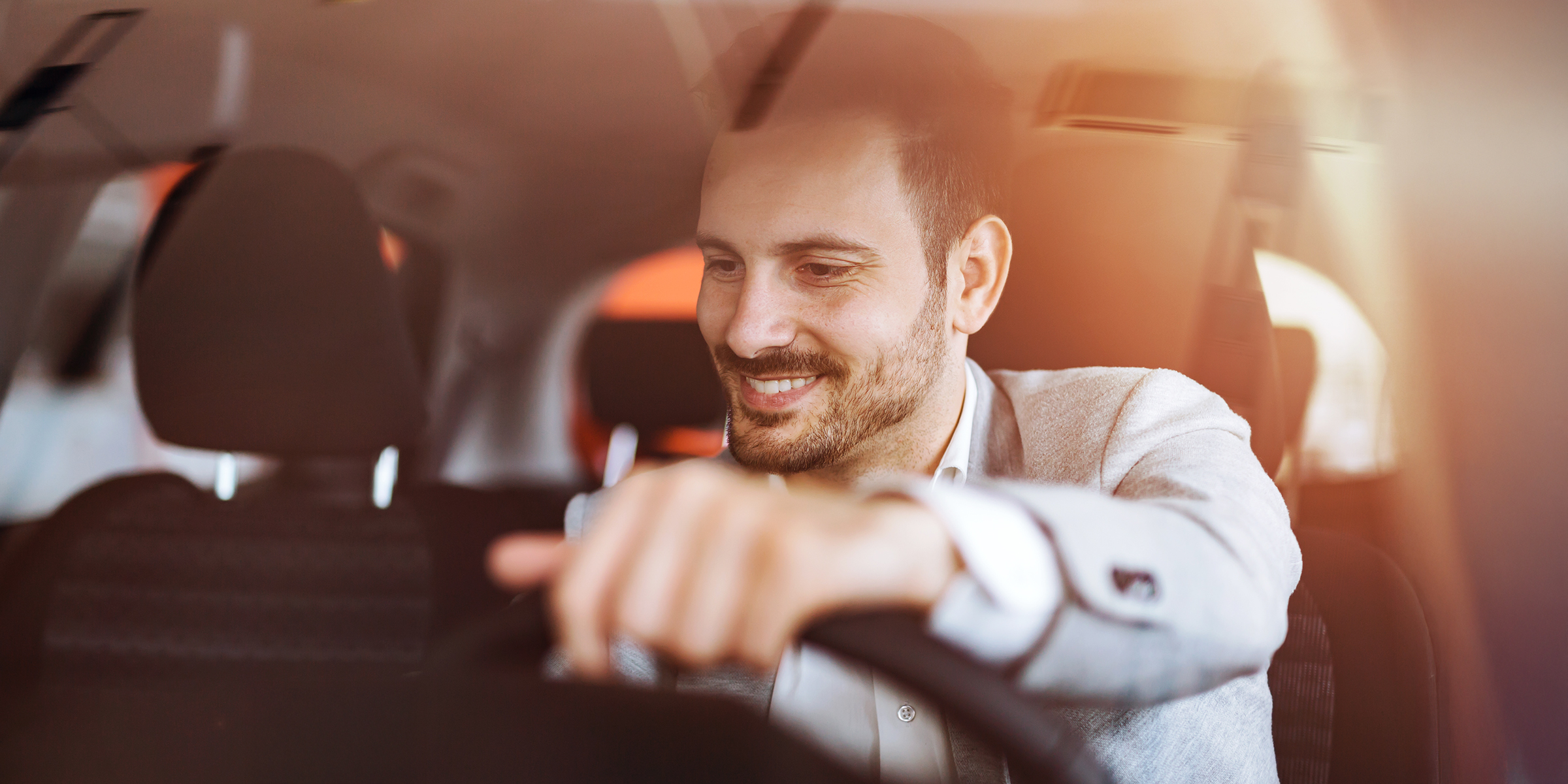 Ein lächelnder Mann sitzt hinter dem Steuer und genießt die Fahrt in seinem Auto | Quelle: Shutterstock
