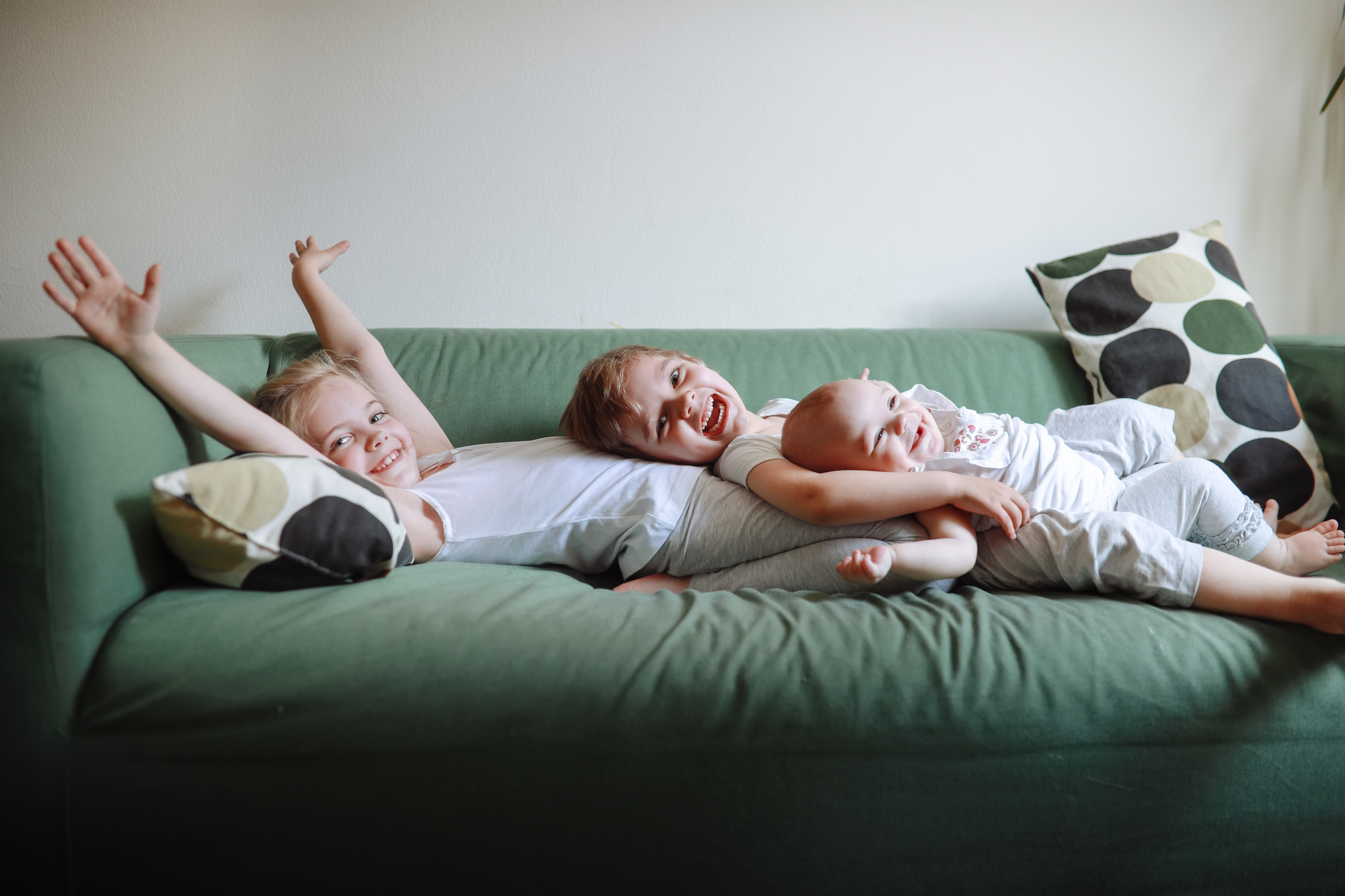 Eine Schwester und zwei kleine Brüder liegen auf einem grünen Sofa | Quelle: Getty Images