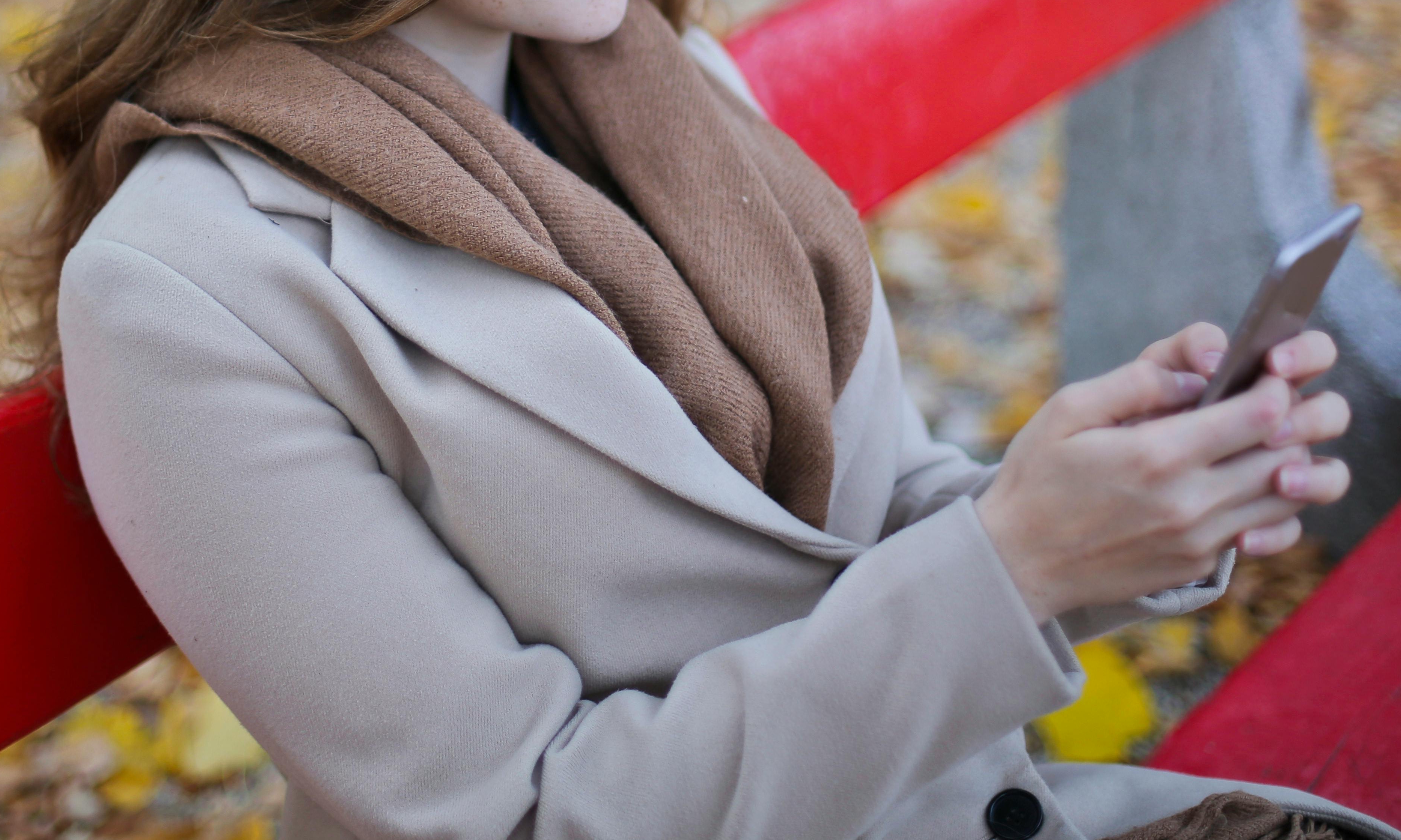 Eine Frau sitzt auf einer Parkbank und hält ein Handy in den Händen | Quelle: Pexels