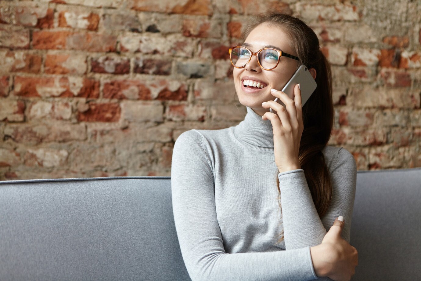 Uma mulher sorridente falando ao telefone e olhando para cima ⏐ Fonte: Freepik