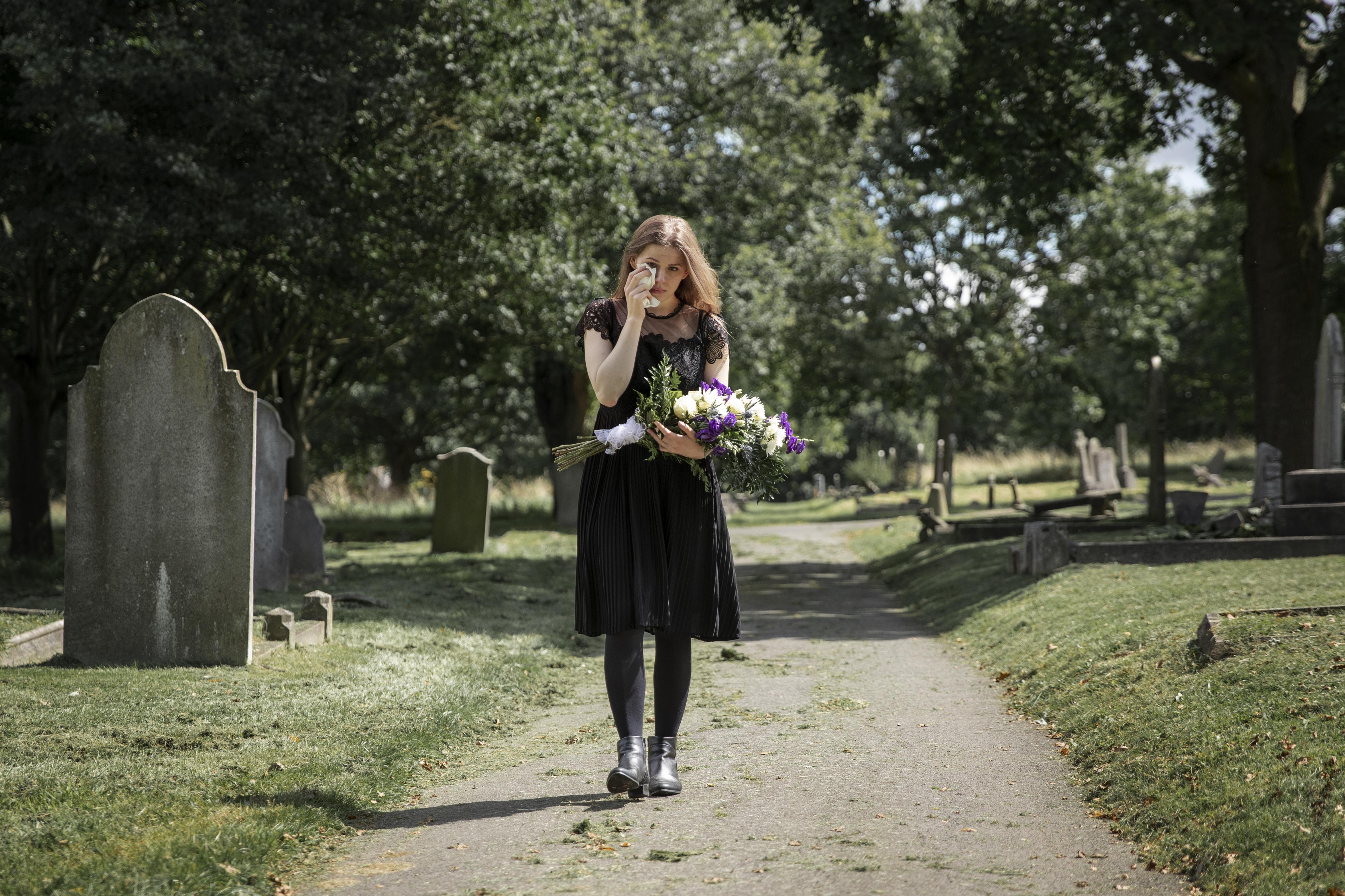 Eine trauernde Frau hält einen Blumenstrauß auf einem Friedhof | Quelle: Freepik