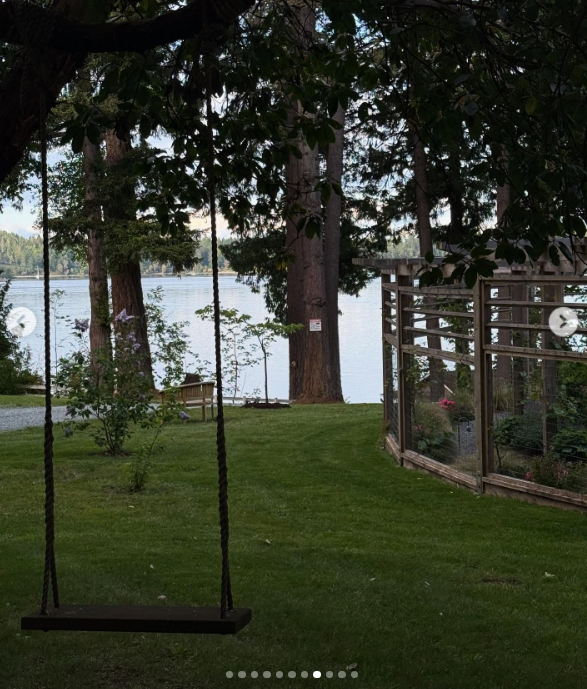 Eine einfache Holzschaukel hängt an einem Ast und bietet einen Blick auf die ruhigen, von Bäumen gesäumten Ufer von Vancouver Island in Arcady. Im Hintergrund rahmen hohe Küsten-Nadelbäume das glitzernde Wasser ein, direkt neben einem umzäunten Garten, der Pamelas Beete schützen soll – so fängt das Bild die gemächliche Ruhe ihres Rückzugsortes am Meer ein. Sie versah das Bild mit der Bildunterschrift: „Ich stelle mir das Leben wie einen Garten vor … Man kann neu pflanzen, von vorne anfangen und ihn zu seinem eigenen machen. 🤍 Liebe, P“. | Quelle: Instagram/pamelaanderson