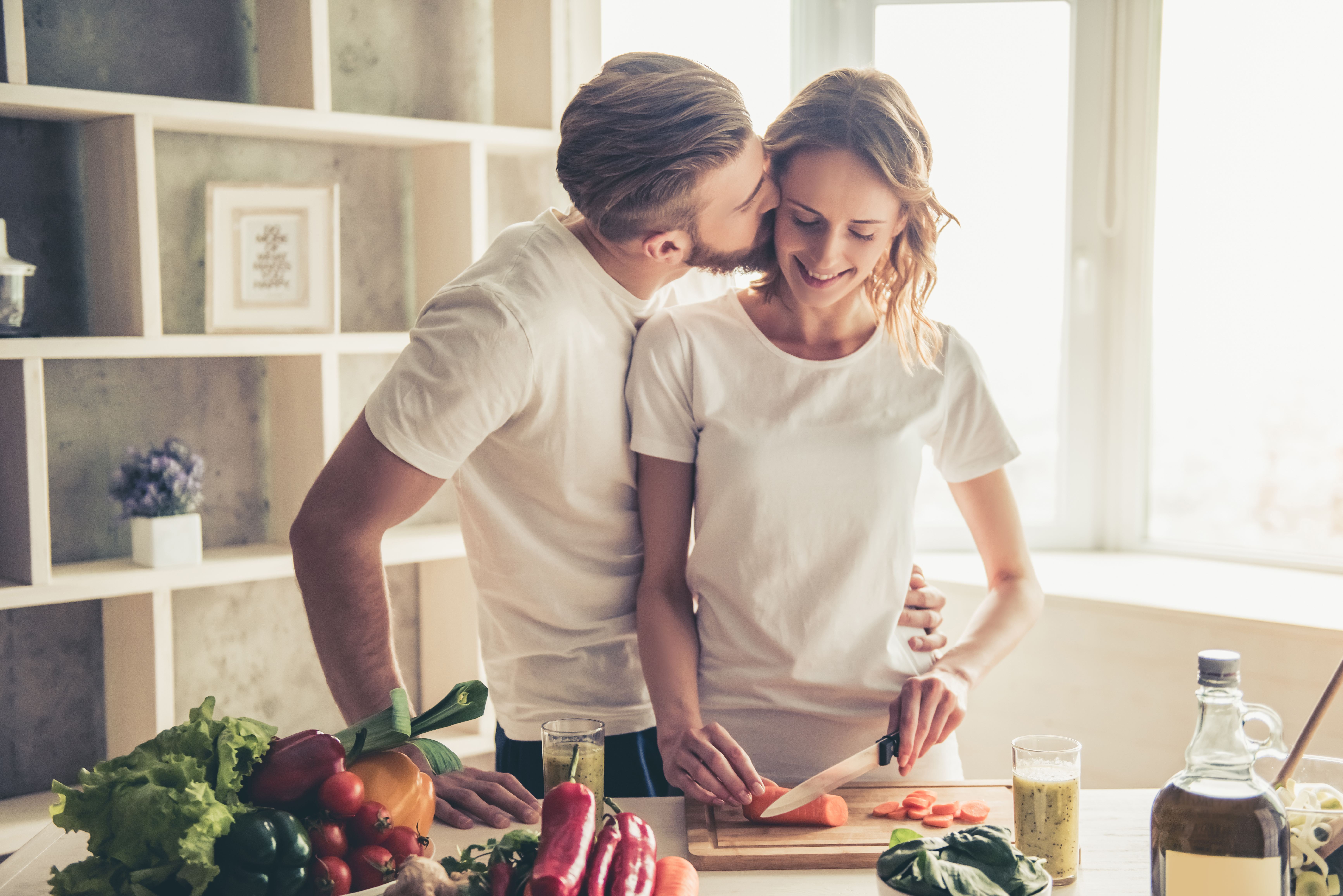 Ein Mann küsst seine Frau, während sie Gemüse schneidet | Quelle: Shutterstock