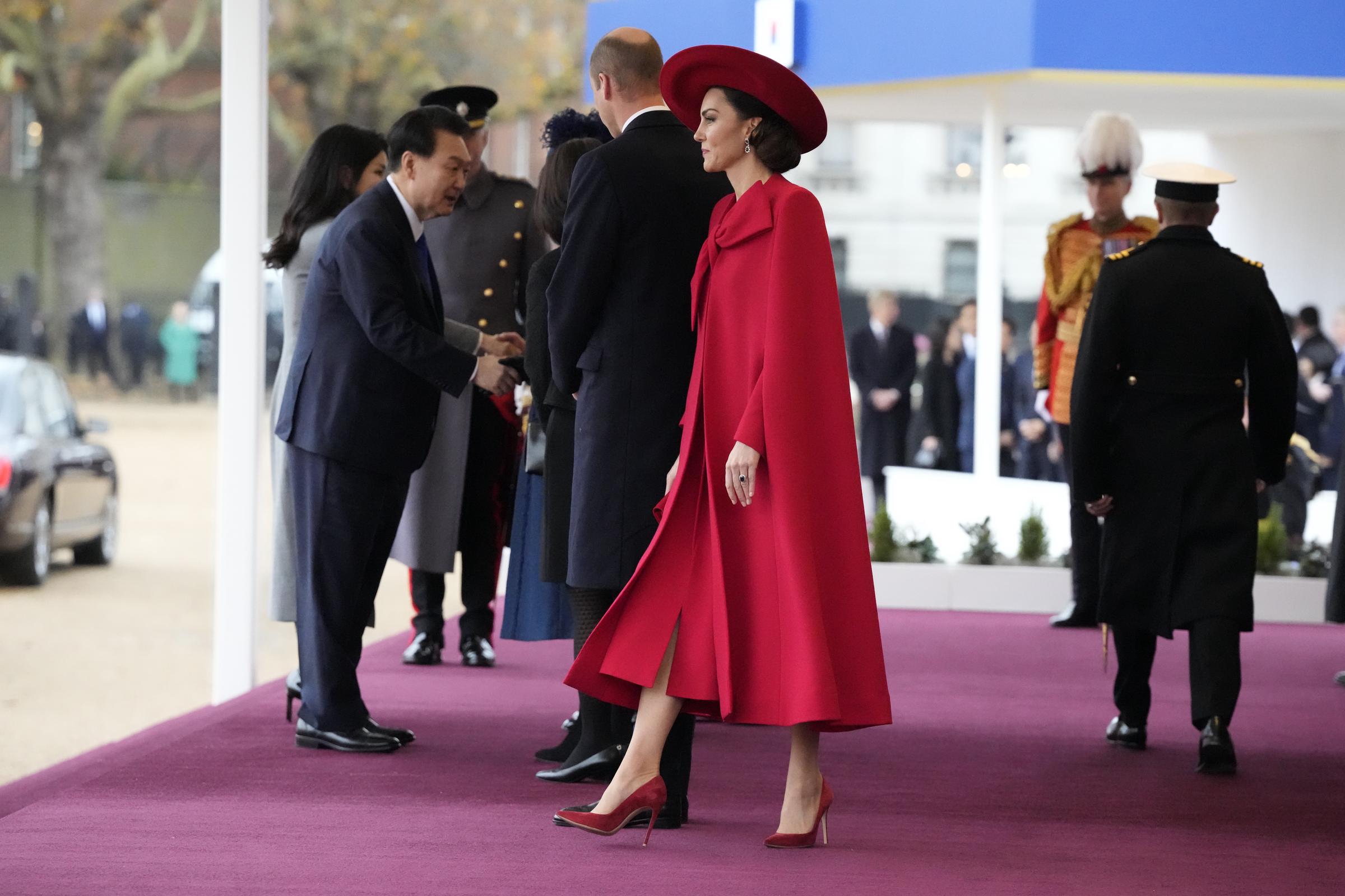 Catherine, Prinzessin von Wales, betritt am 21. November 2023 bei der feierlichen Begrüßung anlässlich des südkoreanischen Staatsbesuchs auf der Horse Guards Parade in London auf dramatische Weise das Podium. Die Königin beherrscht die Bühne in einem ganz in Scharlachrot gehaltenen Outfit: Sie trägt einen maßgeschneiderten Cape-Mantel von Catherine Walker mit einer übergroßen Schleife über einem passenden roten Kleid, dazu einen breitkrempigen Hut von Sarah Cant, Prinzessin Dianas Saphir- und Diamant-Ohrringe sowie rote Wildleder-Pumps von Gianvito Rossi. | Quelle: Getty Images