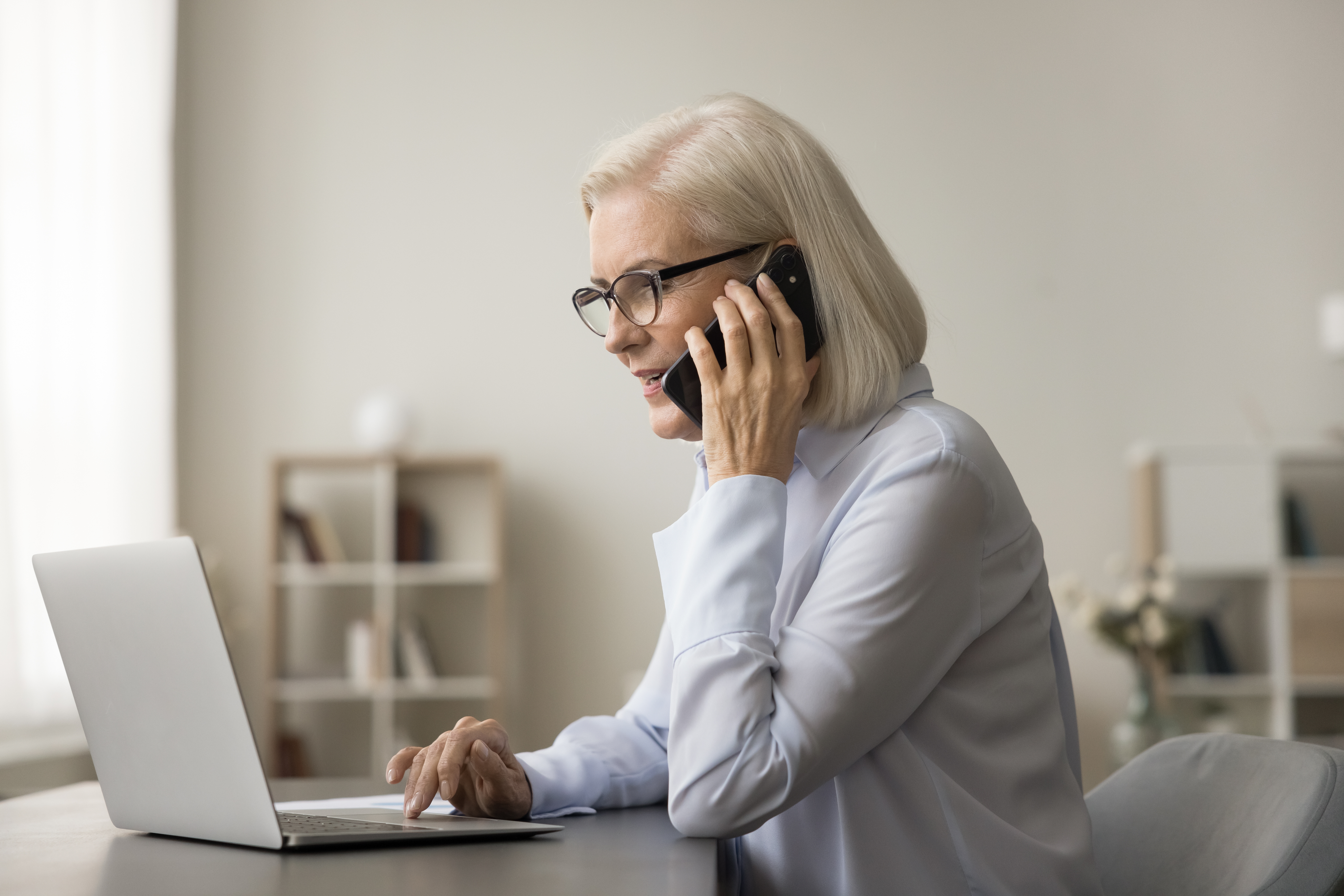 Eine ältere Frau telefoniert und schaut auf einen Laptop | Quelle: Shutterstock