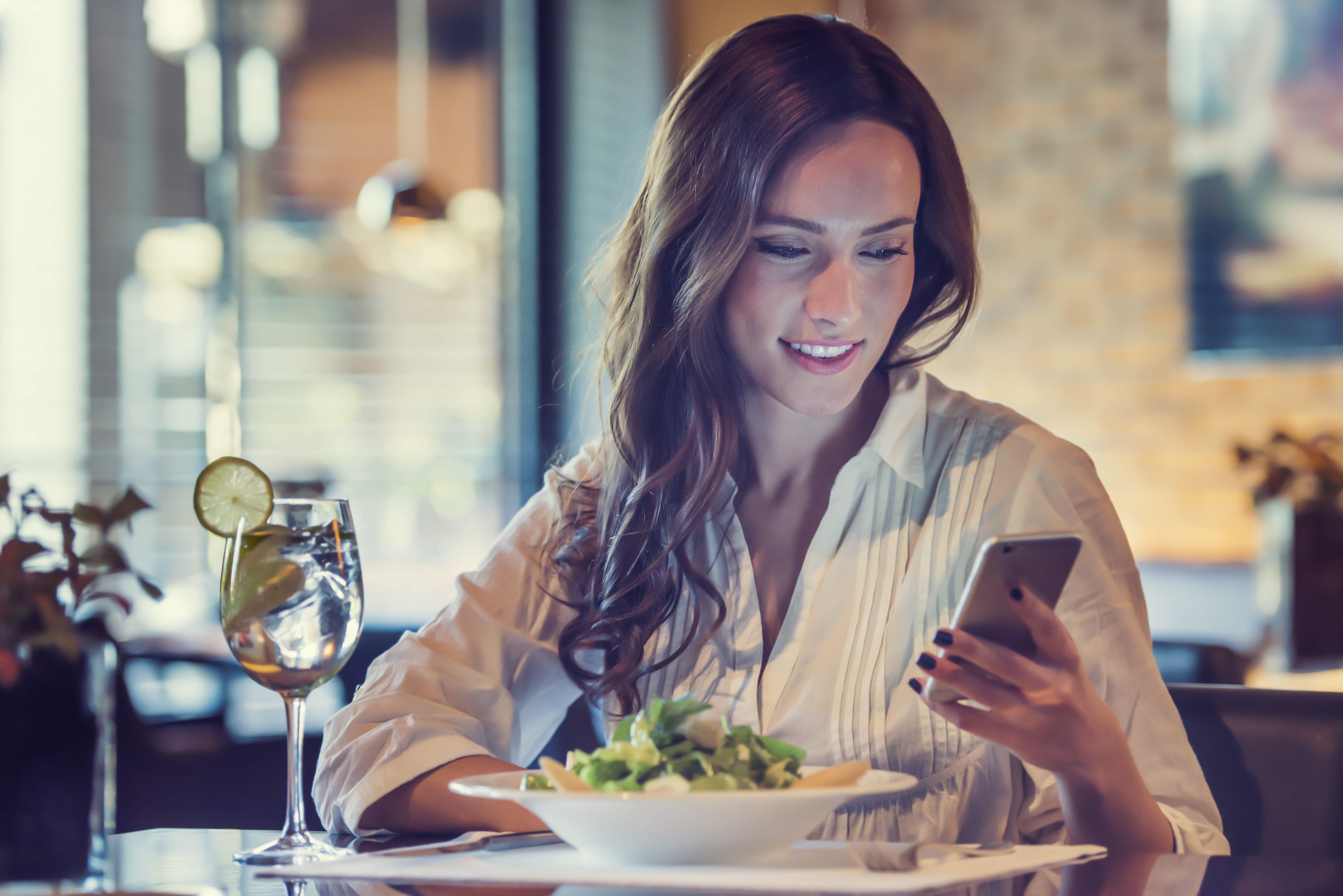 Eine junge Frau benutzt ihr Telefon in einem Restaurant | Quelle: Shutterstock