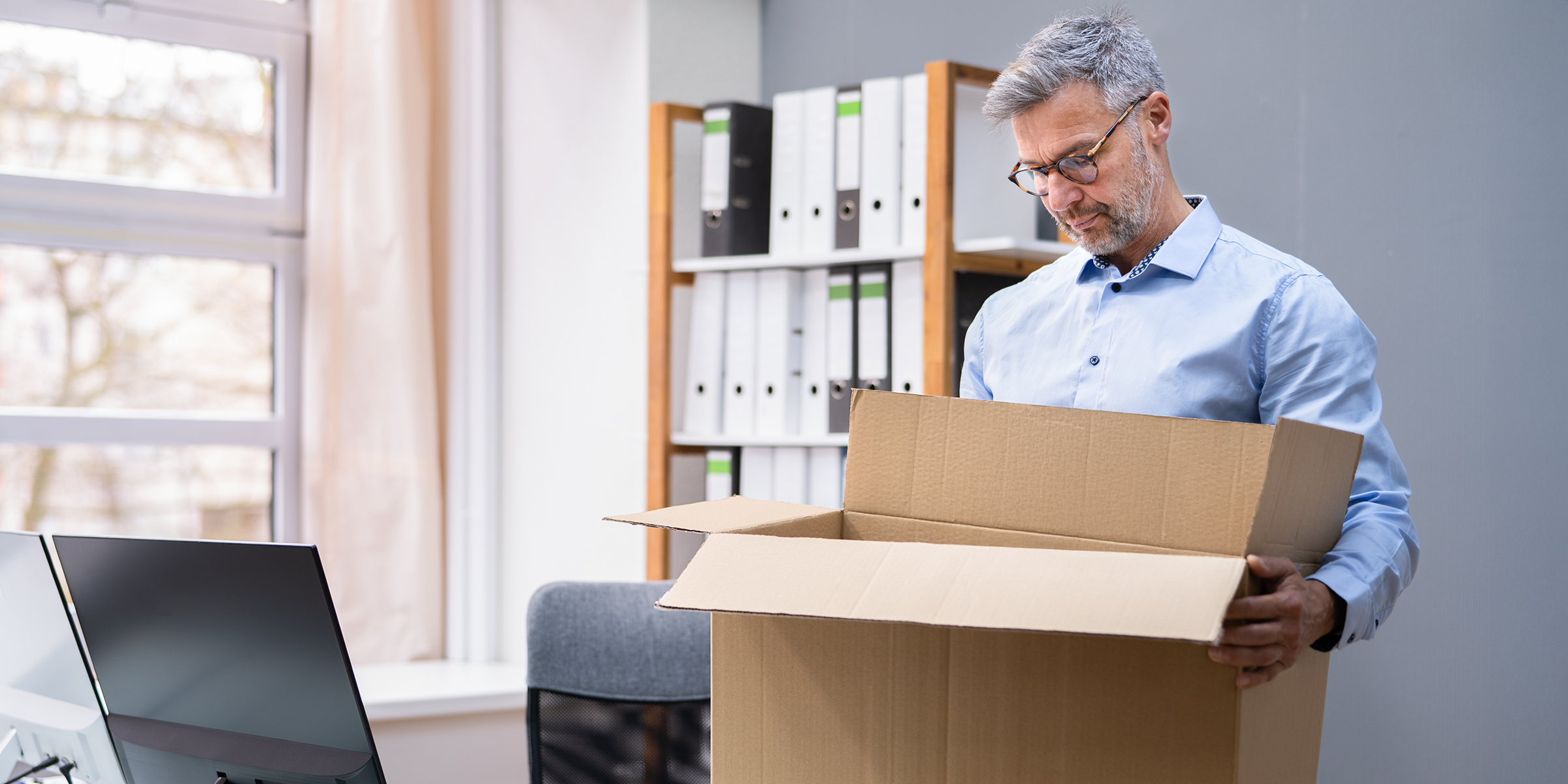Ein Mann steht in seinem Büro und blickt auf einen offenen Karton, während er seine Sachen zusammenpackt | Quelle: Shutterstock