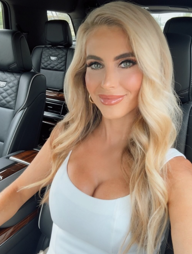 Katie Zacharia posiert für ein Selfie in einem weißen, ärmellosen Top in einem Luxusauto, ihr langes blondes Haar ist zu lockeren Wellen gestylt. Vor ihrer Tätigkeit im Weißen Haus arbeitete sie als Fernsehkommentatorin und hatte verschiedene Positionen in den Bereichen Kommunikation und Recht inne, darunter eine Stelle beim Ministerium für Innere Sicherheit. | Quelle: Instagram/katiezacharia