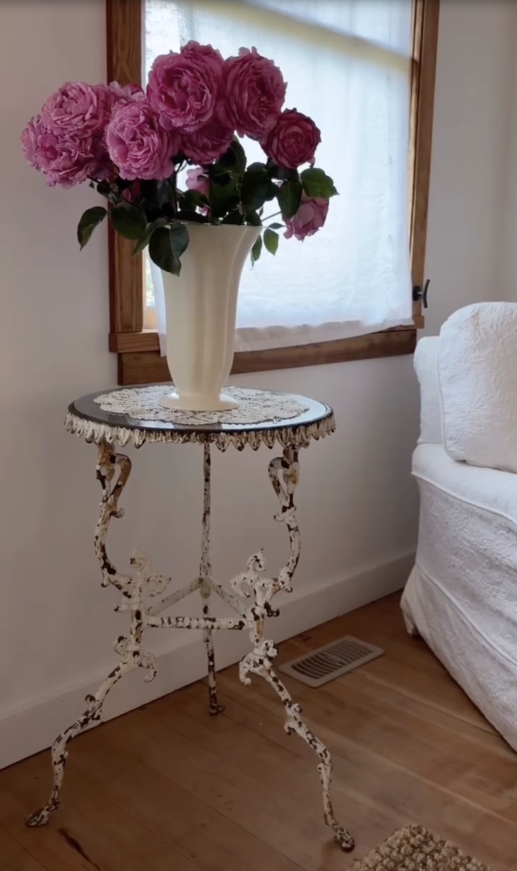 Ein üppiger Strauß frisch geschnittener rosa Yves-Piaget-Rosen steht in einer geriffelten cremefarbenen Keramikvase, die auf einem verzierten, verwitterten Gusseisentisch neben einem sonnendurchfluteten Fenster im „Arcady“ steht. Das blühende Arrangement unterstreicht den romantischen Charme von Pamela Andersons Haus auf Vancouver Island und bringt den üppigen Garten mit klassischer Cottage-Eleganz ins Haus. | Quelle: Instagram/pamelaanderson