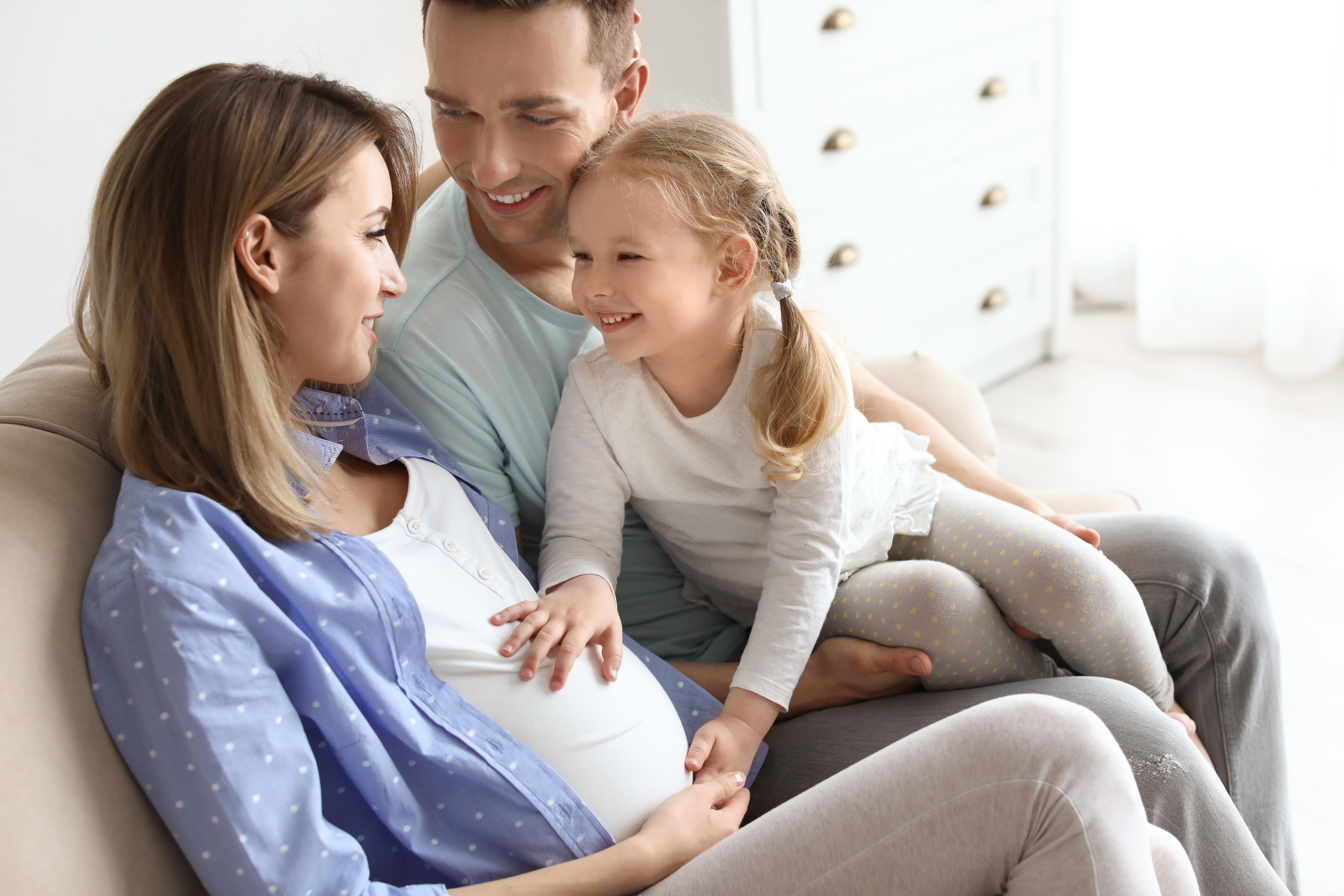 Eine schwangere Frau mit ihrem Mann und ihrer kleinen Tochter zu Hause | Quelle: Shutterstock