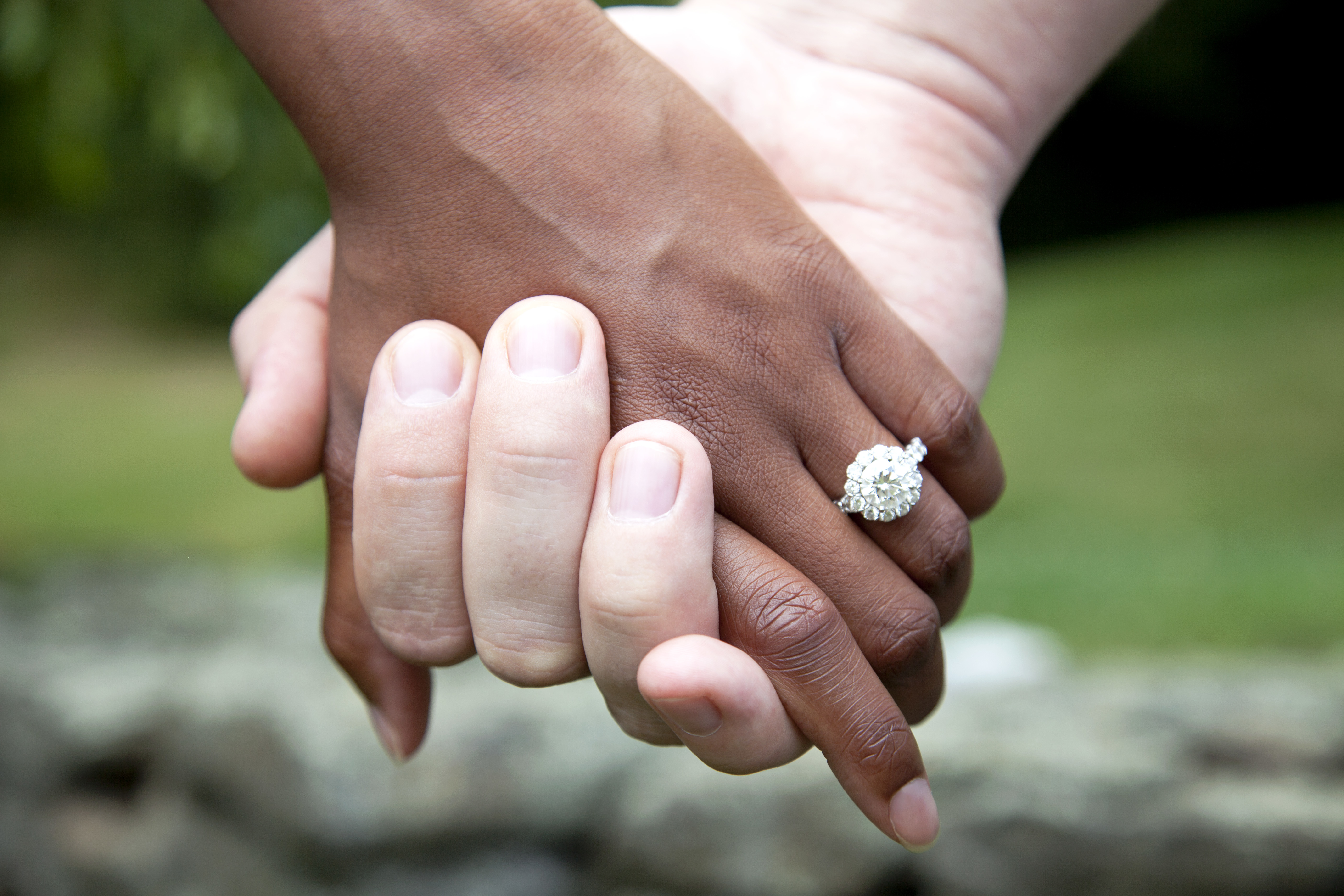 Ein gemischtrassiges Paar hält Händchen und trägt einen diamantenen Verlobungsring, Nahaufnahme | Quelle: Getty Images