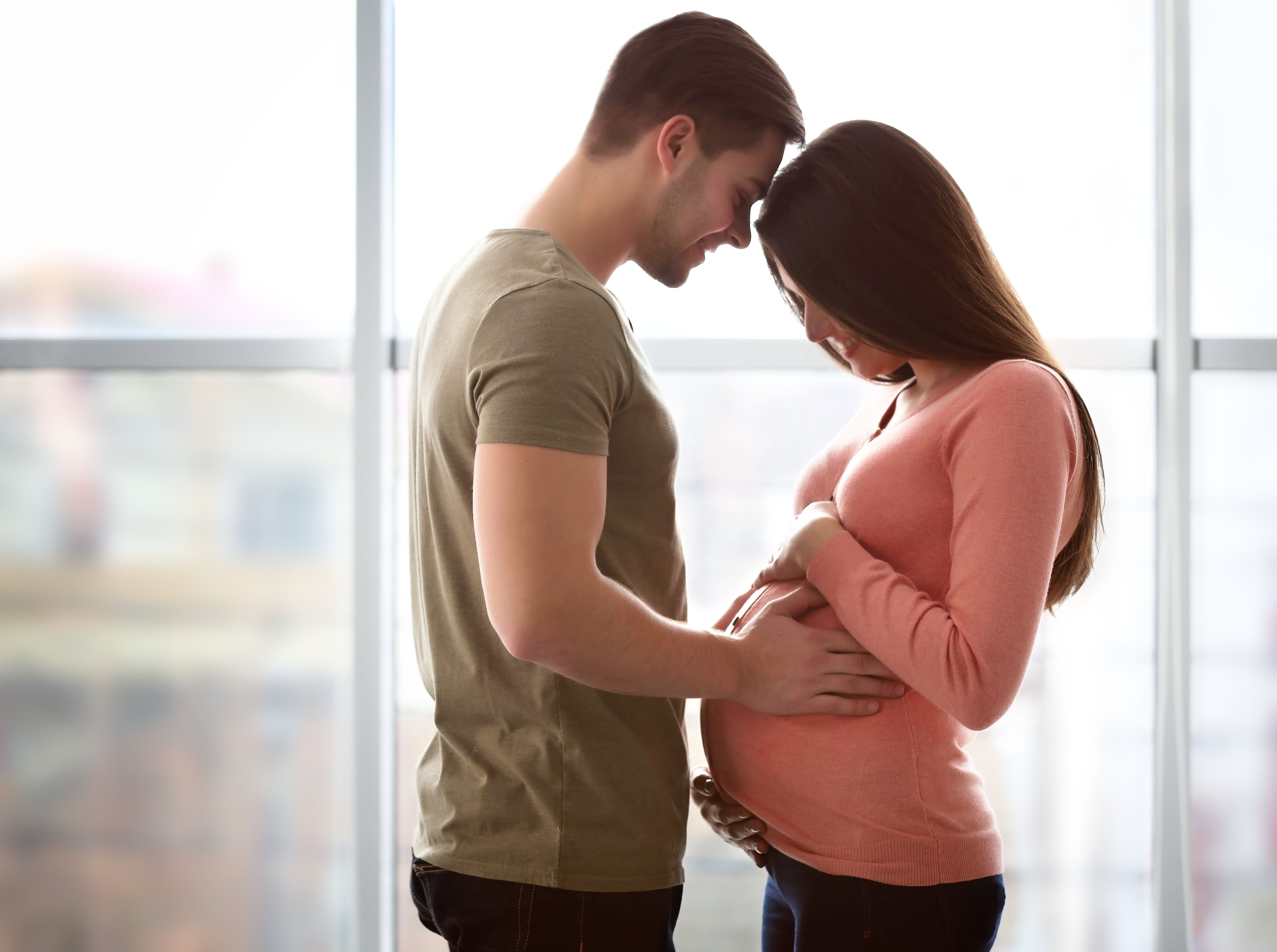 Eine Frau schaut auf ihren schwangeren Bauch hinunter, während ihr Mann seine Stirn auf ihrer ruht | Quelle: Shutterstock