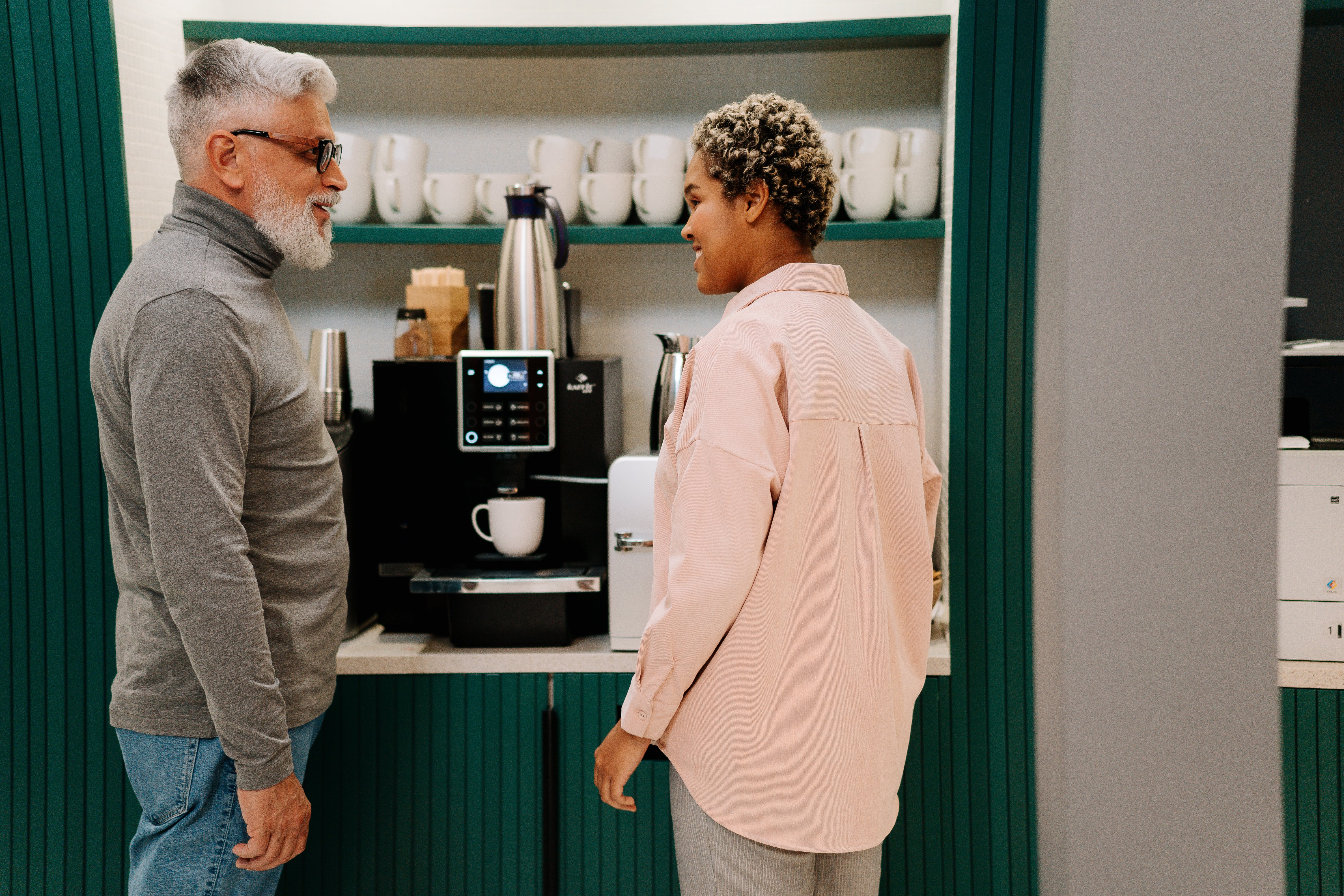 Ein älterer Mann spricht mit einer jüngeren Frau, während er vor einer Kaffeemaschine steht | Quelle: Pexels