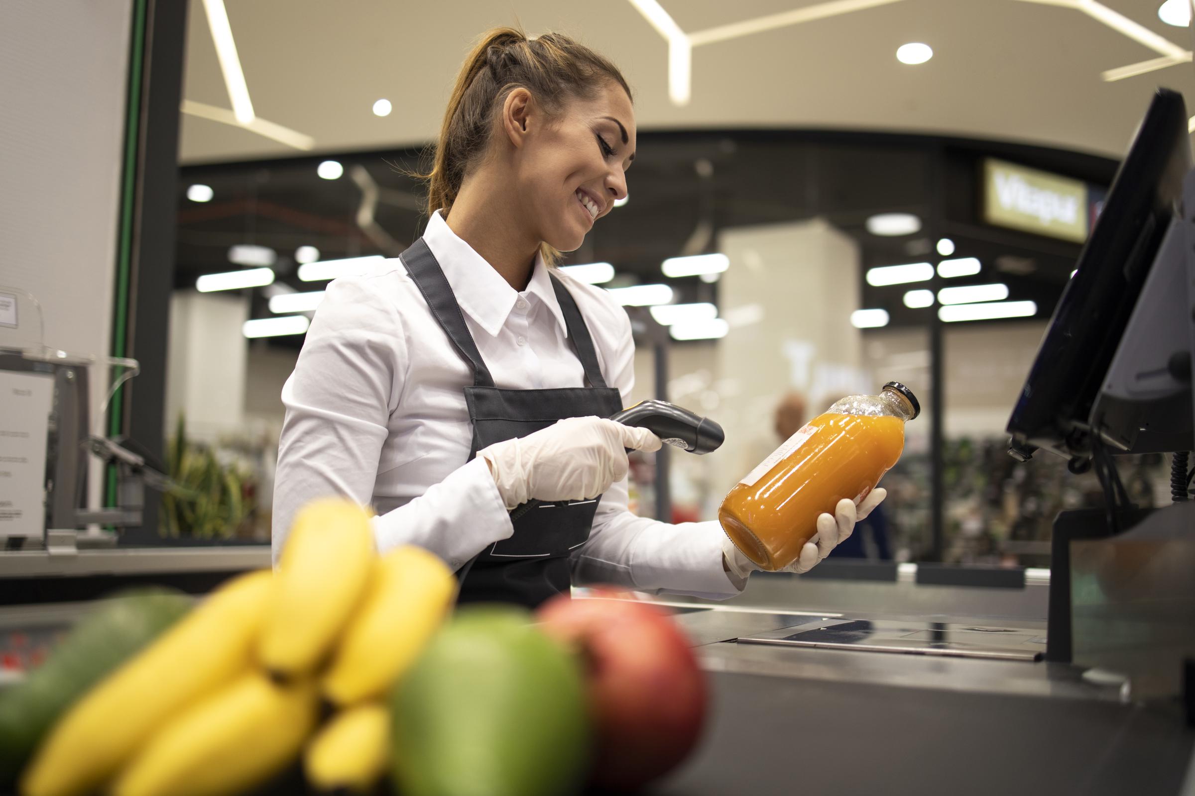 Porträt einer Kassiererin im Supermarkt, die die Barcodes der zum Verkauf stehenden Produkte einscannt | Quelle: Magnific