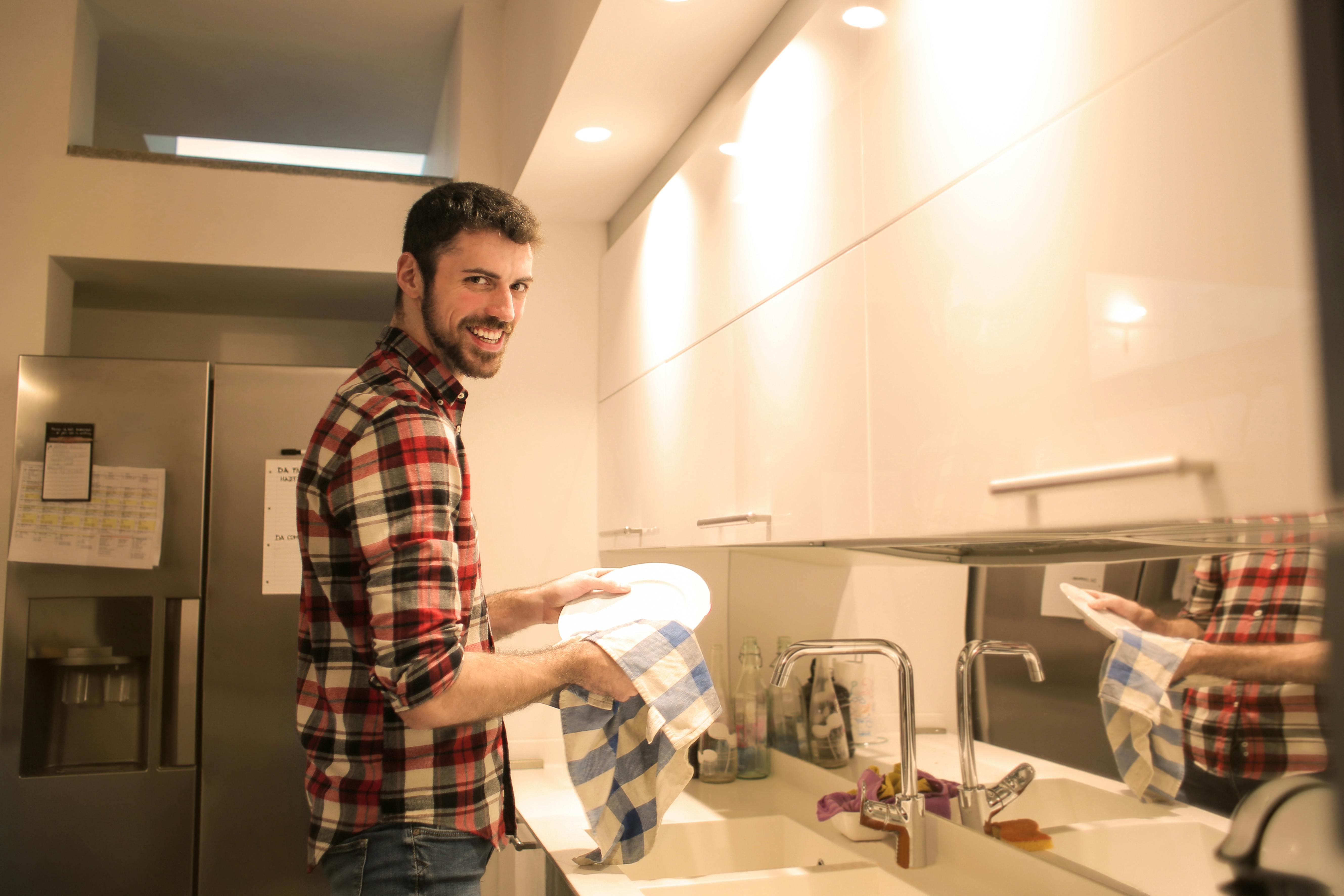 Mann lächelt beim Abwasch | Quelle: Pexels