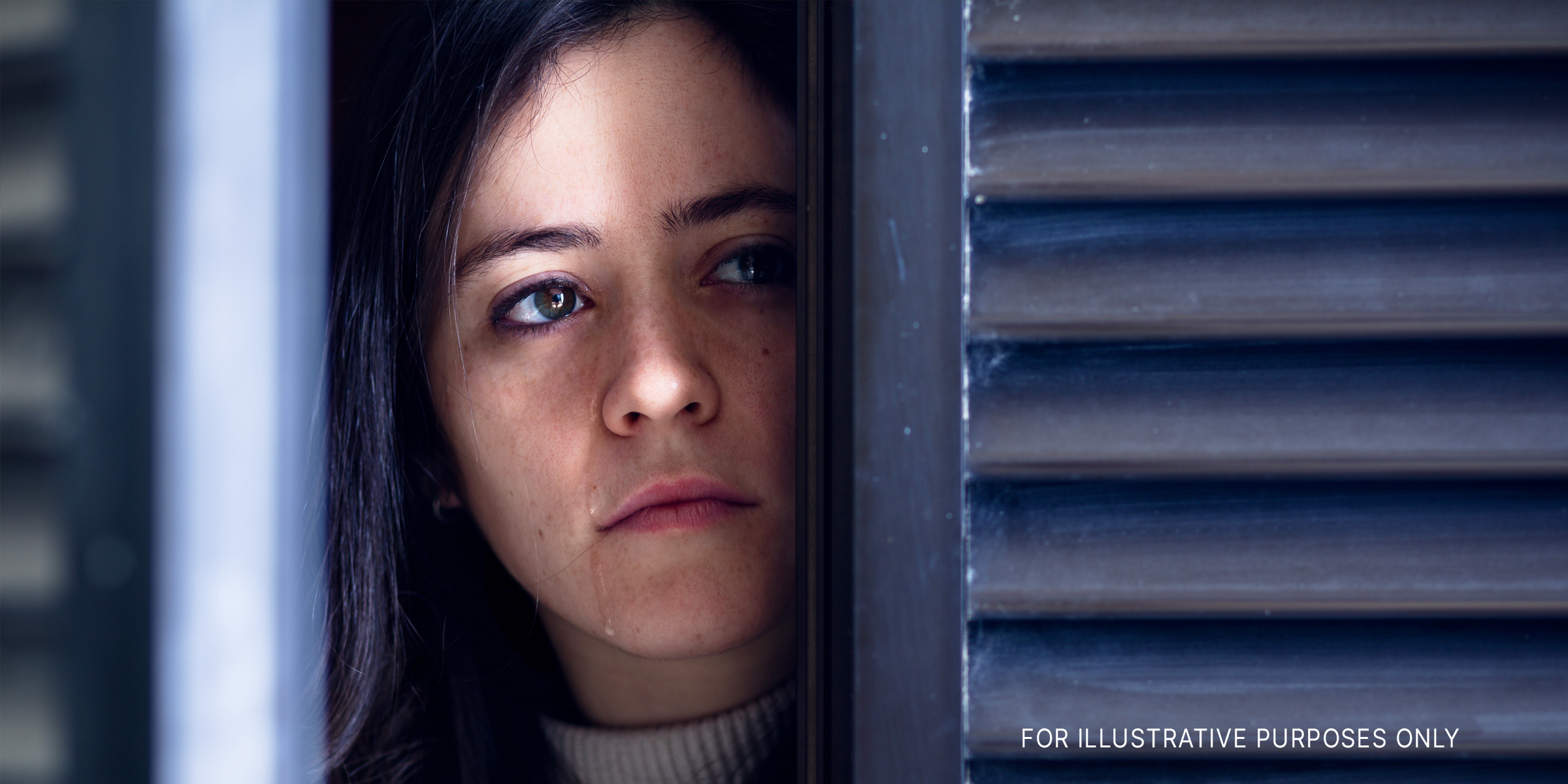 Eine Frau, die durch eine Tür/Fenster schaut und weint | Quelle: Shutterstock