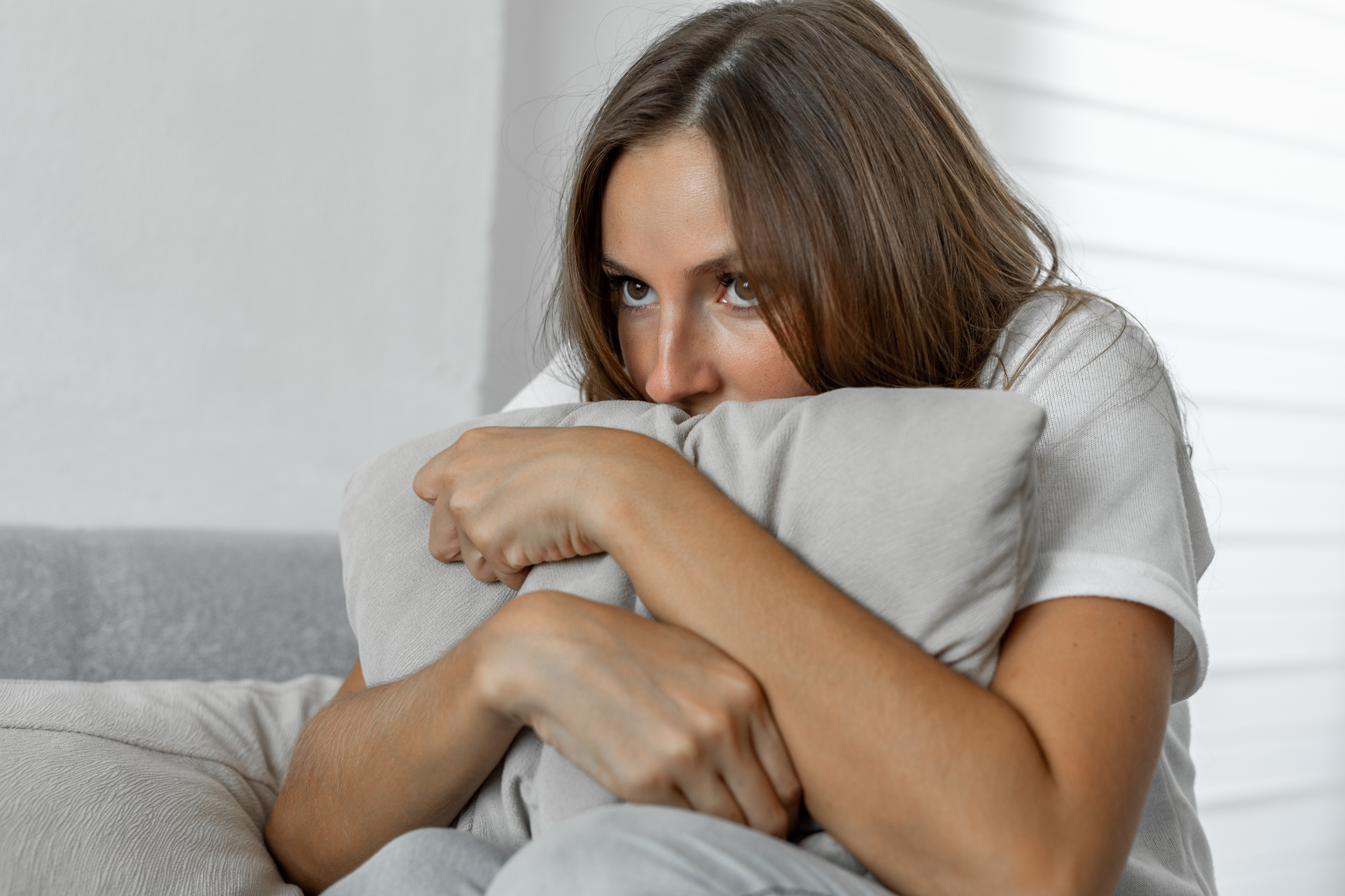 Verängstigte Frau zu Hause, die ein Kissen umarmt, das auf einem Sofa liegt | Quelle: Getty Images