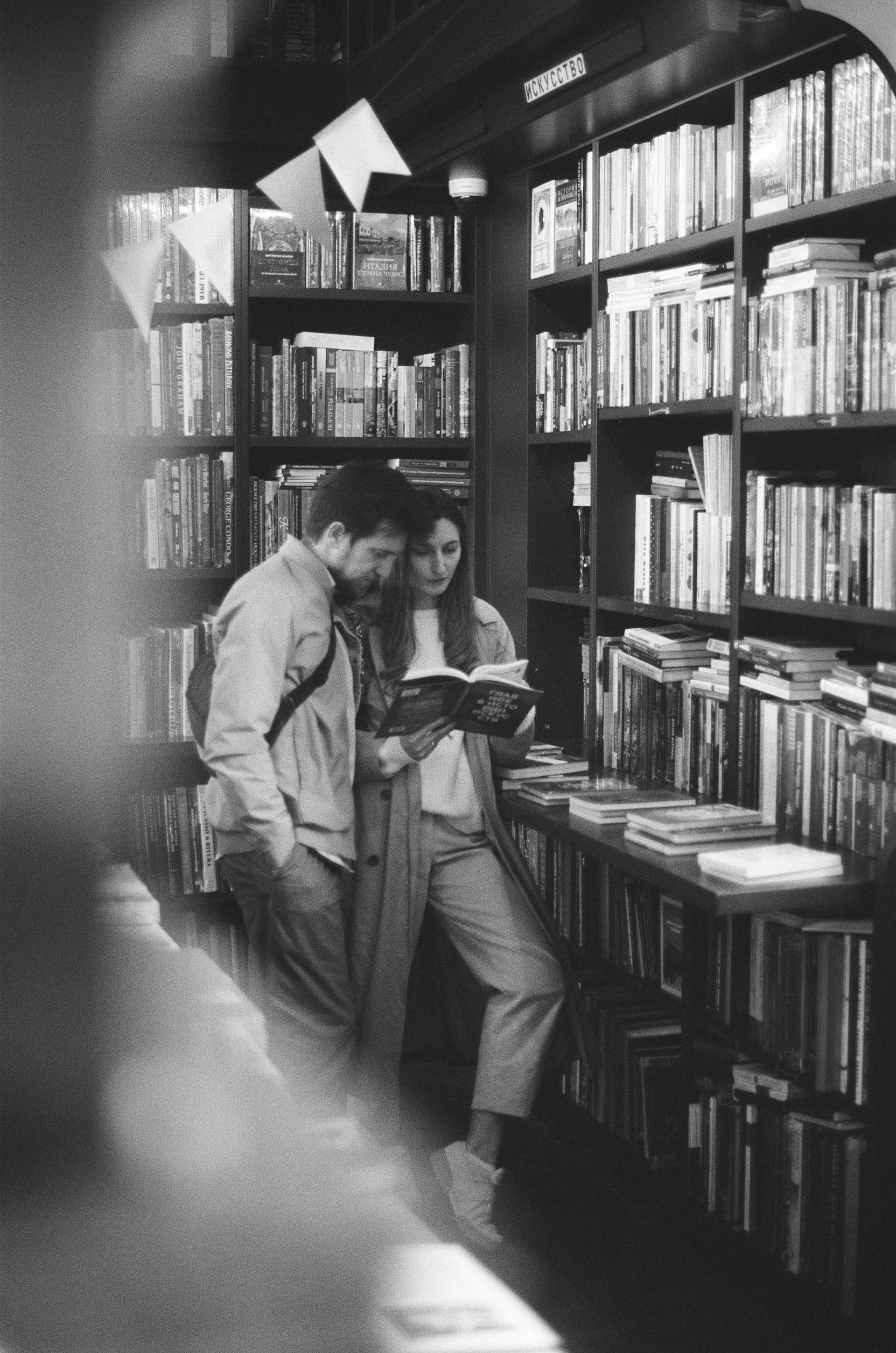 Ein Graustufenfoto von einem Paar, das ein Buch in einer Bibliothek liest | Quelle: Pexels