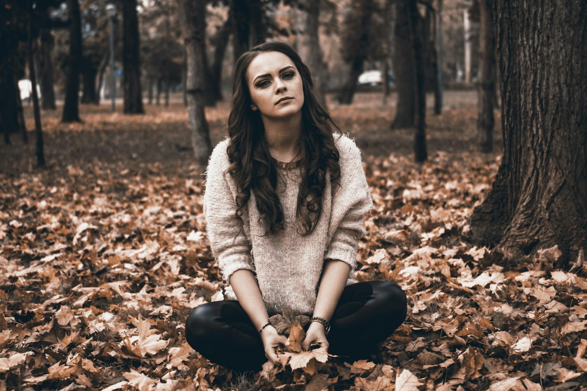 Eine junge Frau, die in einem Wald sitzt und heruntergefallene Blätter hält | Quelle: Pexels