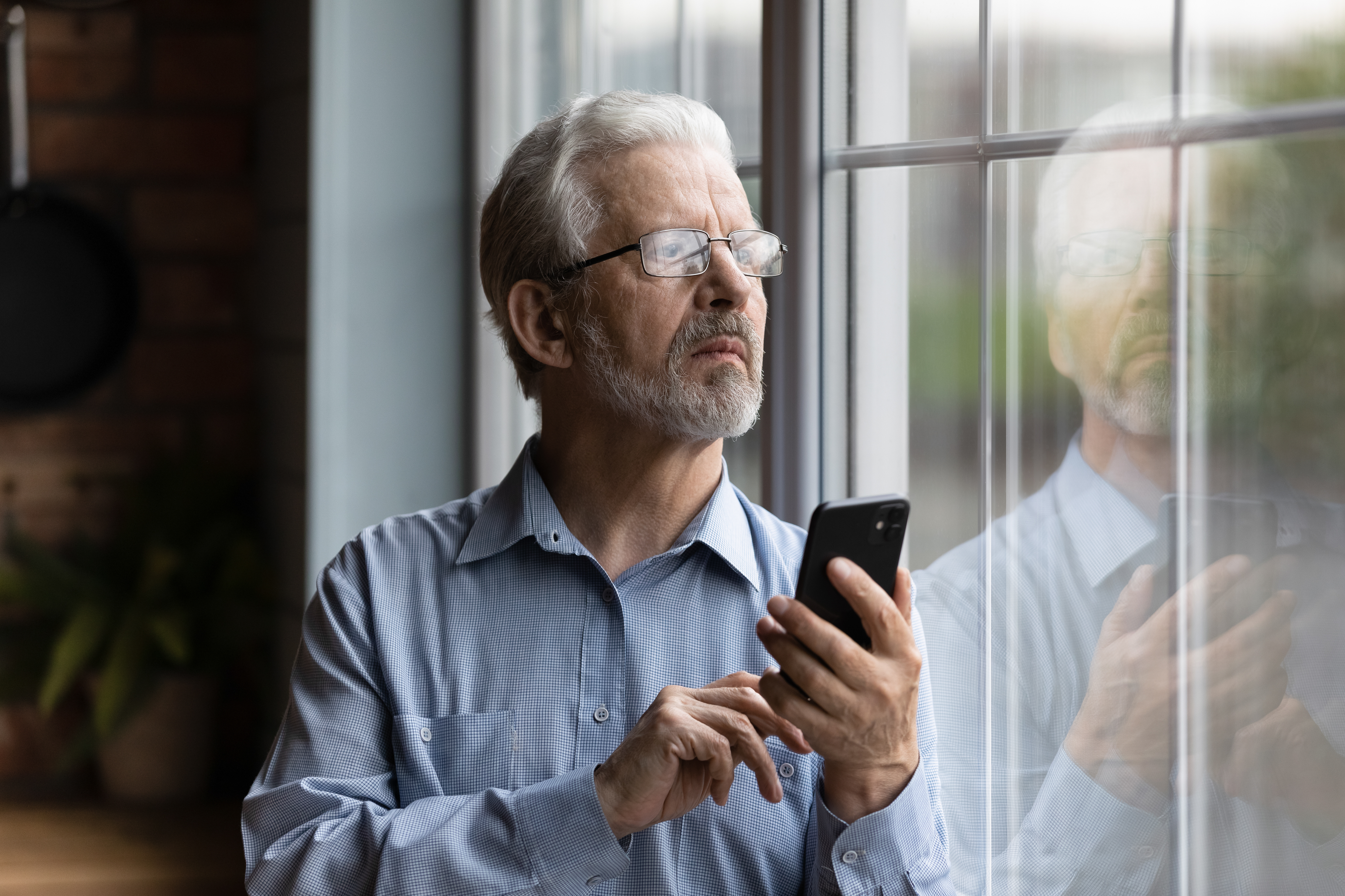 Ein Mann, der mit einem Telefon in der Hand aus einem Fenster schaut | Quelle: Shutterstock