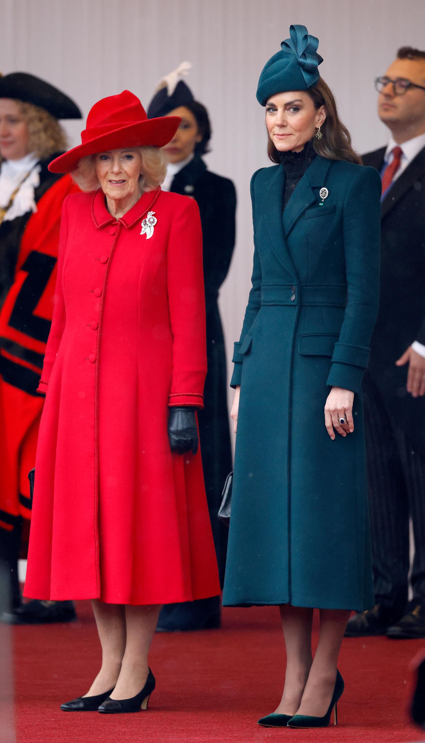 Catherine, Prinzessin von Wales, steht am 20. Oktober 2026 in Windsor neben Königin Camilla auf dem roten Teppich. Im auffälligen Kontrast zu Camillas leuchtend rotem, ausgestelltem Mantel und dem dazu passenden Hut mit Krempe trägt Catherine ein smaragdgrünes Midi-Mantelkleid mit markant strukturierten Schultern, kombiniert mit einem passenden, kunstvoll geformten Fascinator, schwarzen Spitzendetails am Ausschnitt und grünen Samt-Pumps mit spitzer Zehenpartie. | Quelle: Getty Images