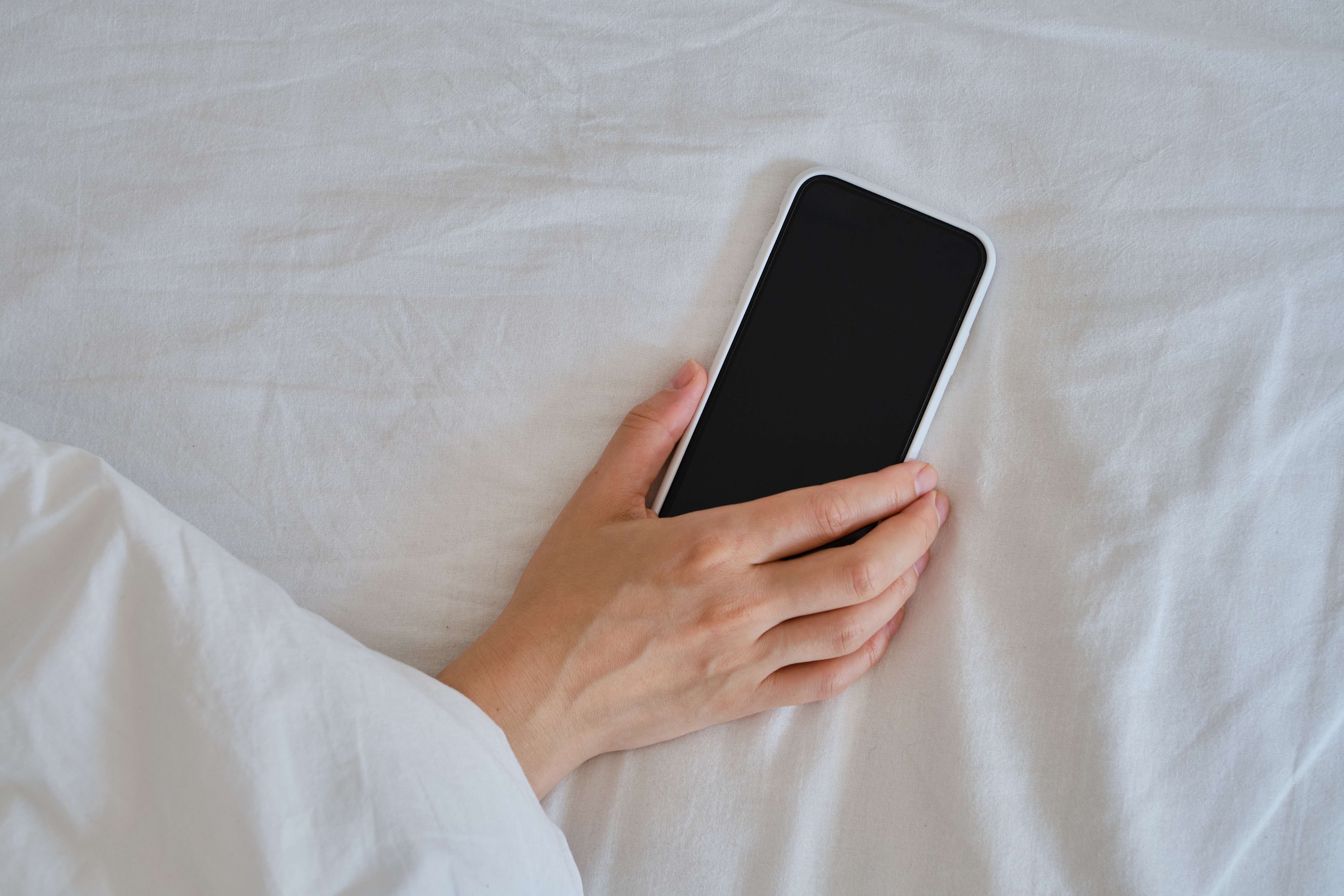 Nahaufnahme einer Hand, die ein Smartphone im Bett hält | Quelle: Shutterstock