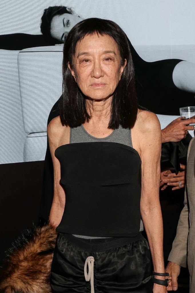 Diese KI-generierte Visualisierung zeigt Vera Wang mit einem geraden Mikro-Pony und glattem, dunklem Haar, wobei realistische Gesichtszüge und ein nicht retuschiertes Profil hervorgehoben werden. Vor einem monochromen Interieur-Hintergrund verbindet das simulierte Styling lässige Streetwear-Elemente mit Abendglamour: ein trägerloses schwarzes Oberteil über einem melierten grauen Sport-Tanktop und geraffte Kleidungsstücke mit Kordelzug. | Quelle: Gemini