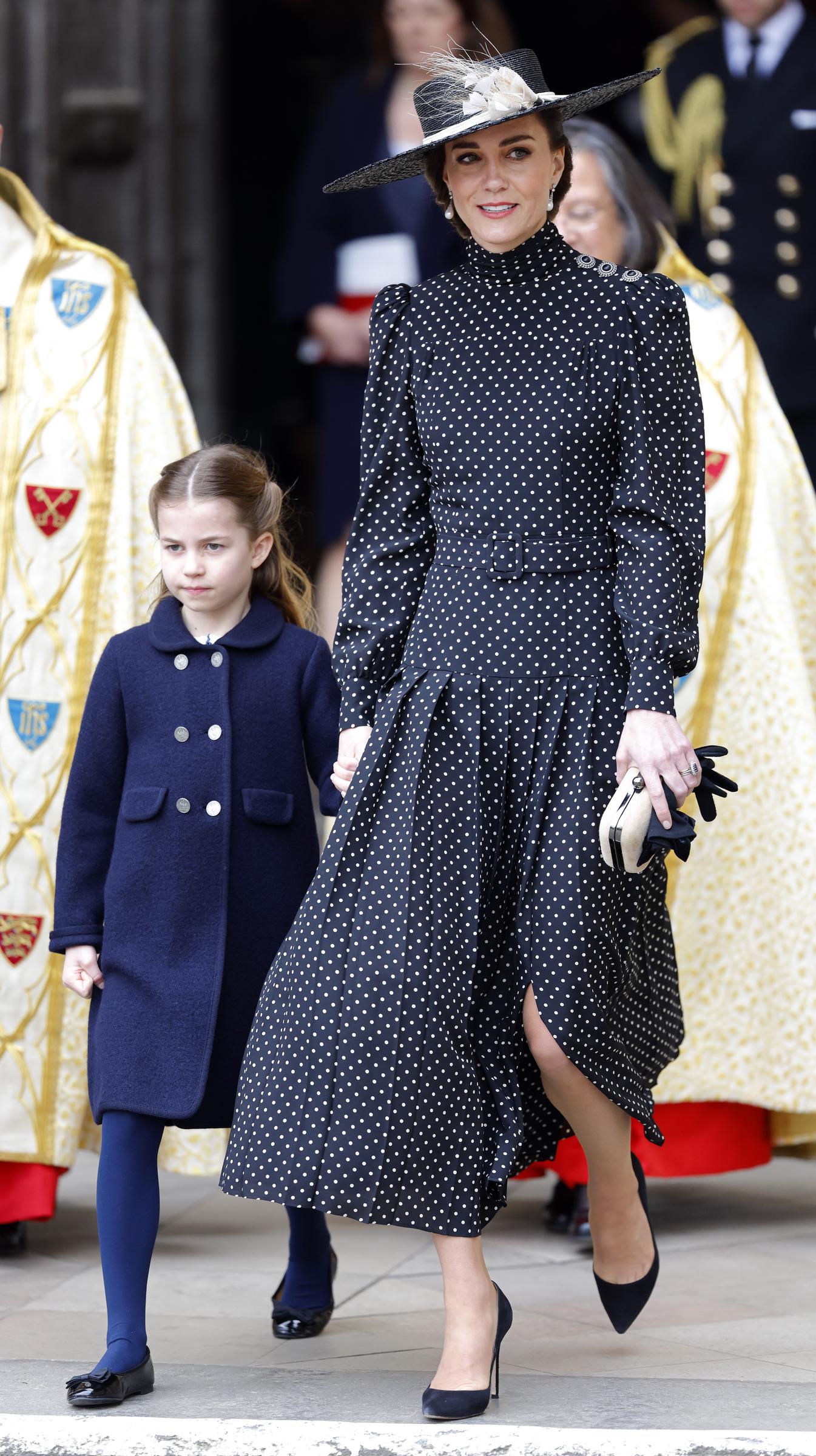 Prinzessin Charlotte geht Hand in Hand mit Catherine, Herzogin von Cambridge, als sie am 29. März 2022 in London, England, nach dem Dankgottesdienst für das Leben von Prinz Philip, Herzog von Edinburgh, die Westminster Abbey verlassen. Charlotte trägt einen marineblauen Mantel mit Knöpfen über einer passenden Strumpfhose und schwarzen Lackschuhen und hält Catherine an der Hand, die ein elegantes schwarz-weiß gepunktetes Midikleid mit Falten, einen breitkrempigen Hut mit floralen Akzenten und spitze schwarze Pumps trägt. | Quelle: Getty Images