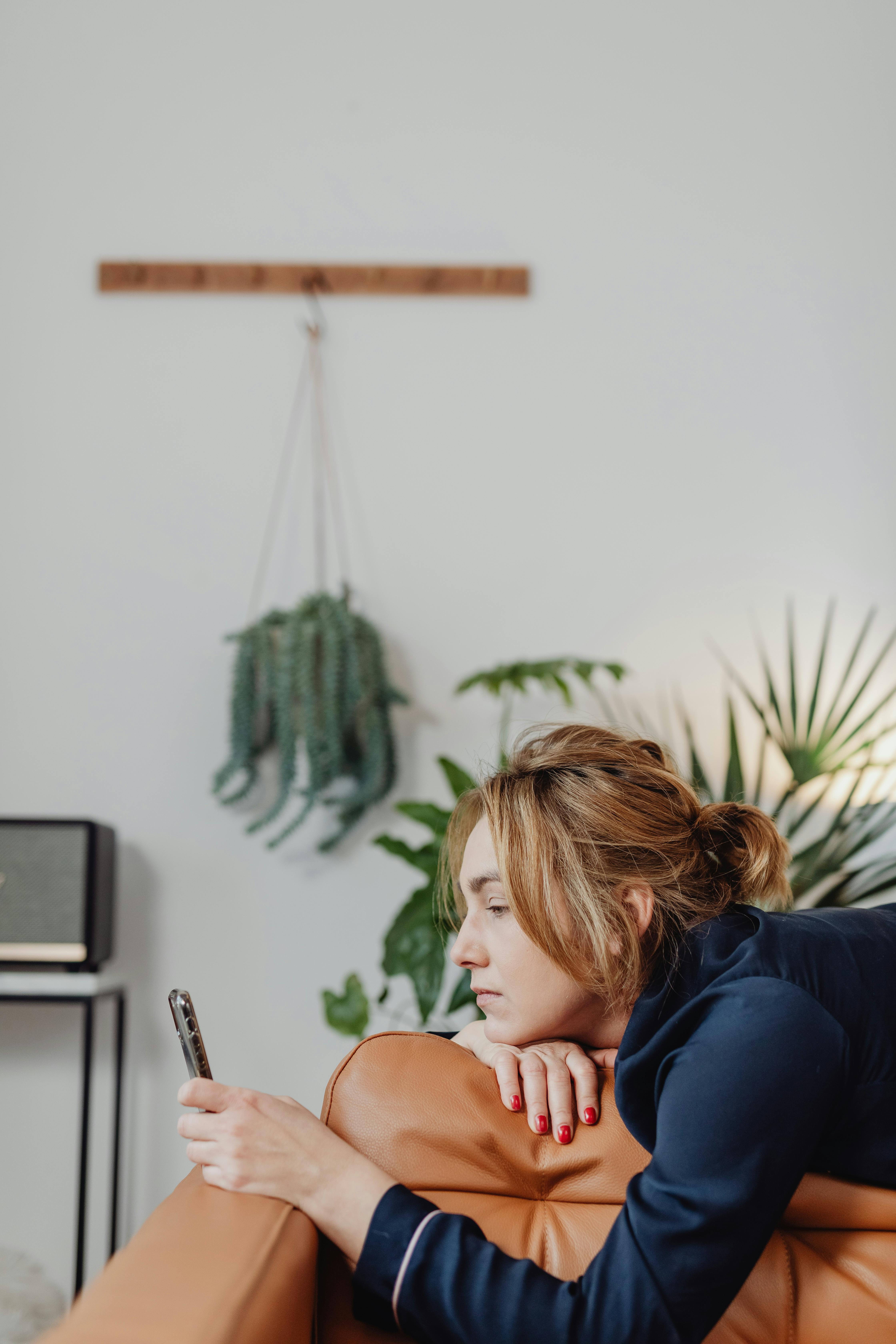 Frau, die auf einer braunen Ledercouch liegt und auf ihr Handy schaut | Quelle: Pexels