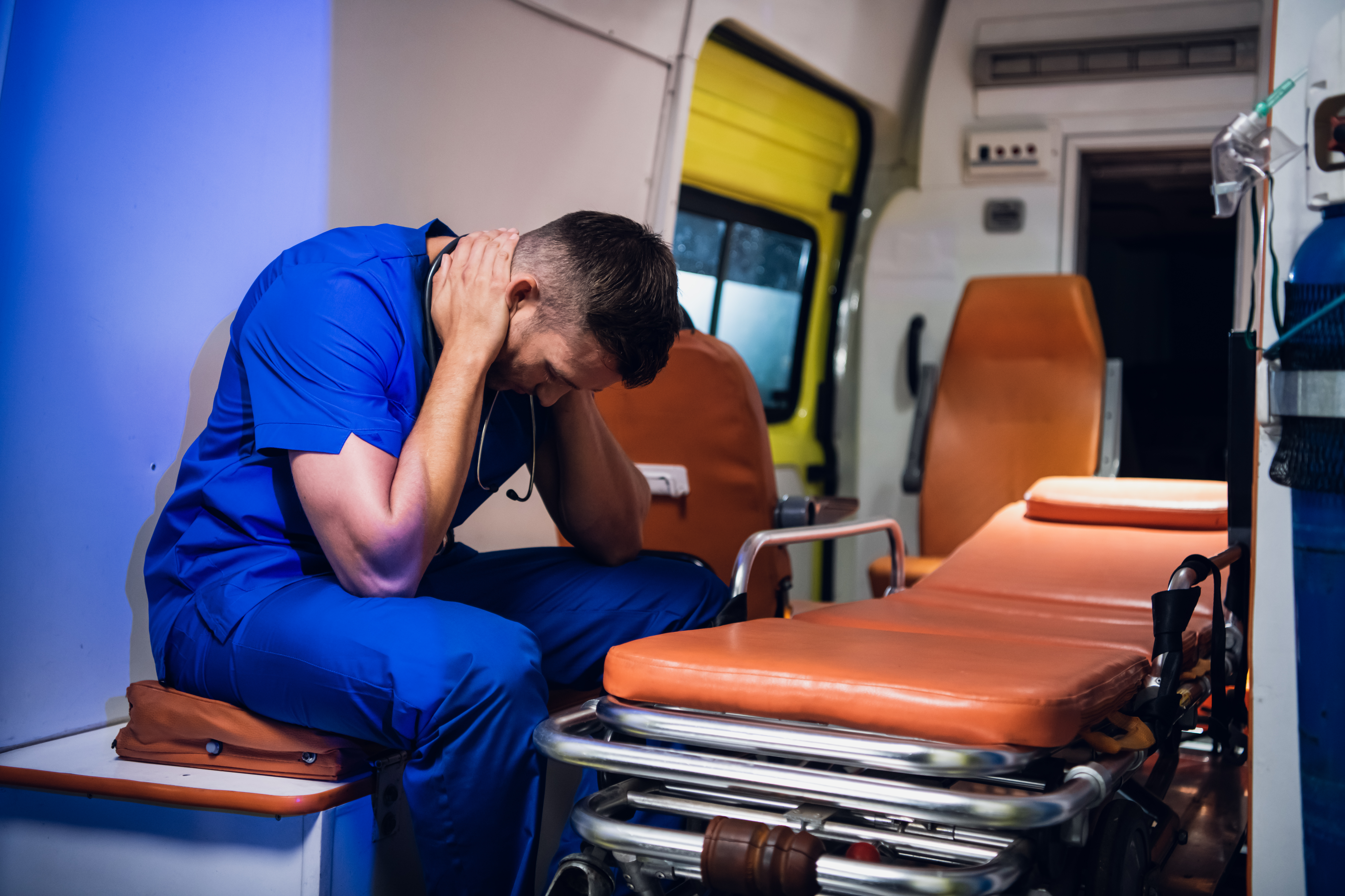 Ein erschöpfter Sanitäter, der sich eine kleine Pause gönnt, indem er in einem Krankenwagen sitzt und die Hände um den Hals legt | Quelle: Shutterstock