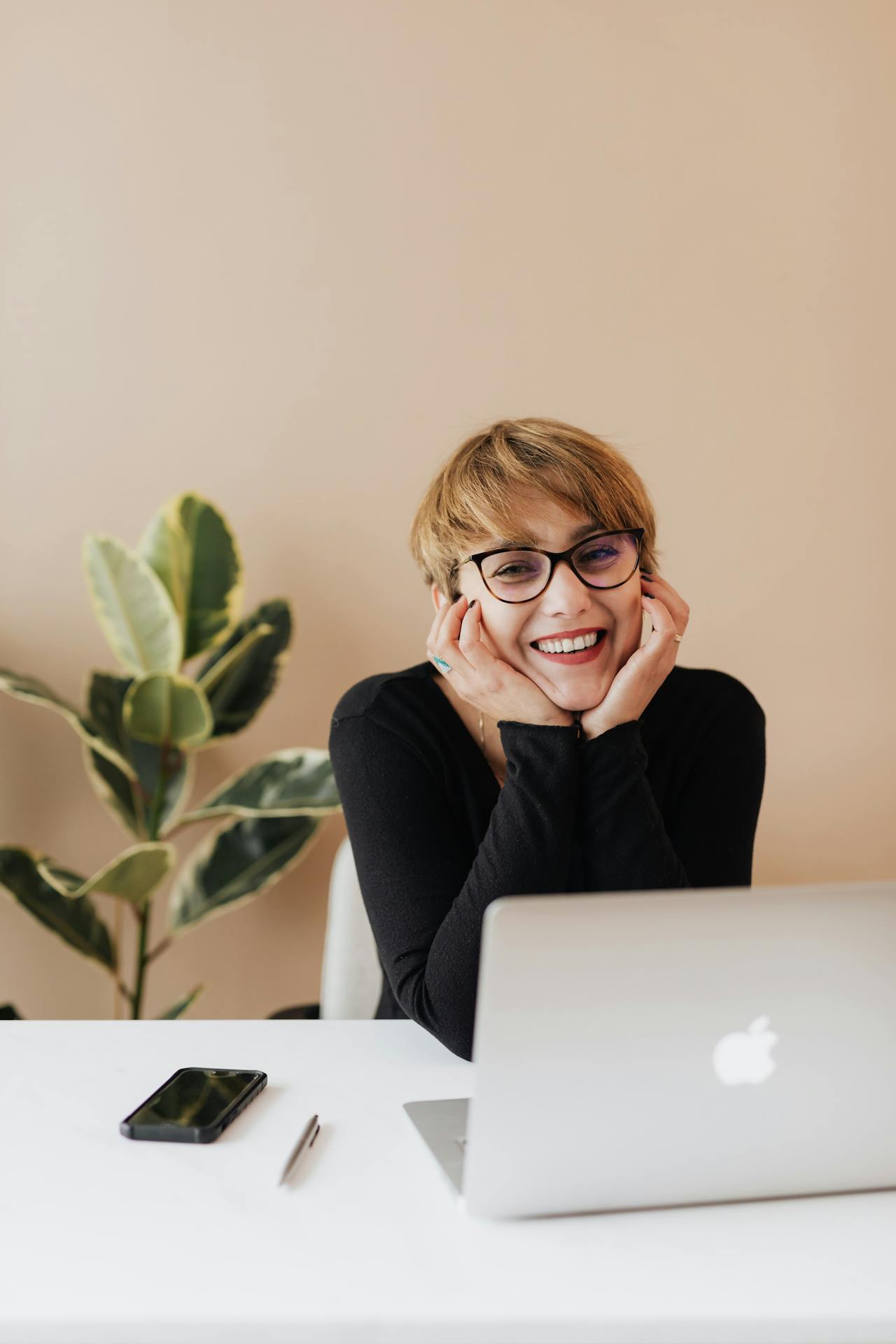 Eine Frau lächelt, während sie mit ihrem Laptop an einem Tisch sitzt | Quelle: Pexels