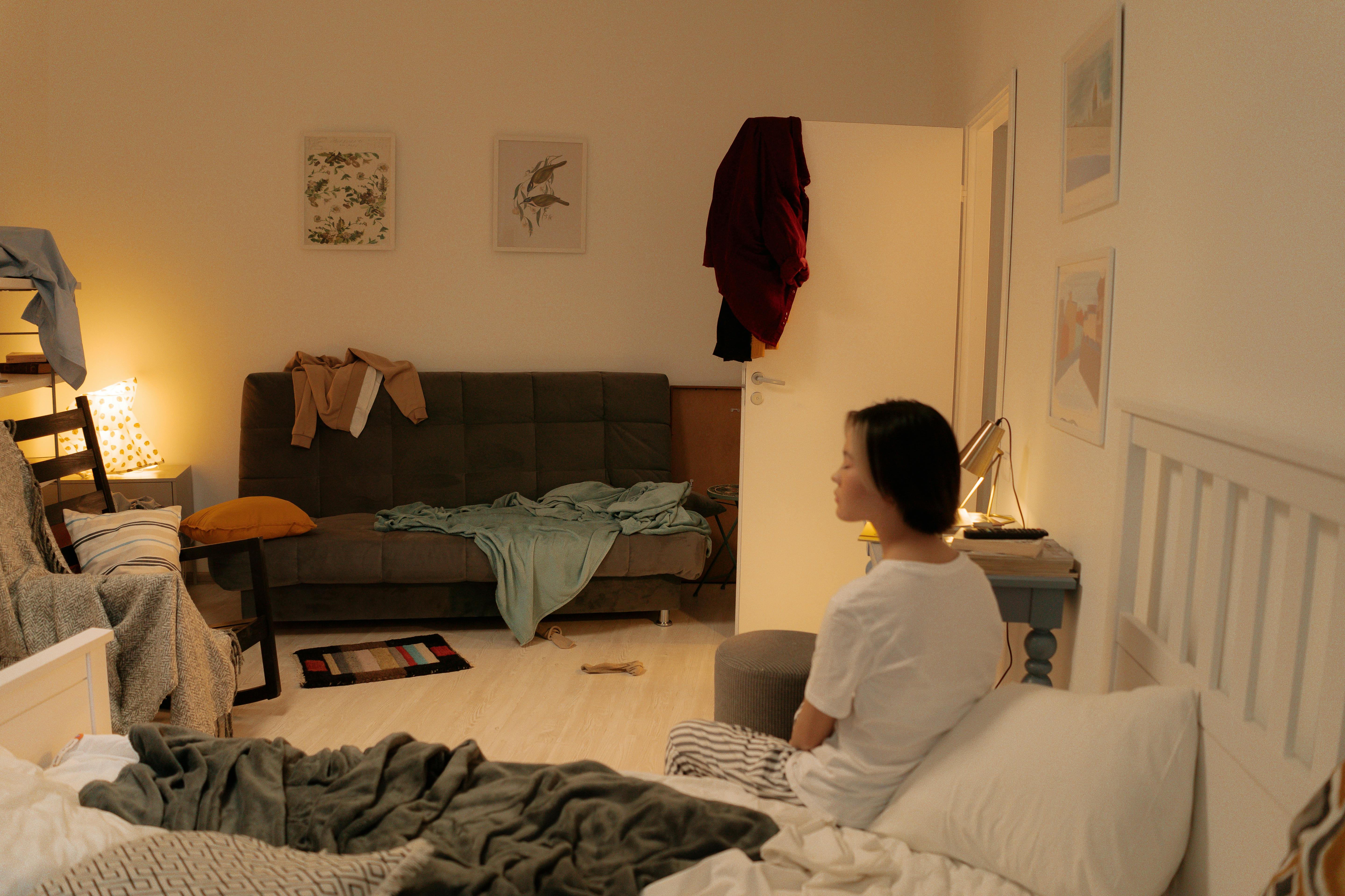 Ein unordentliches Schlafzimmer mit einer Frau, die auf dem Bett sitzt | Quelle: Pexels