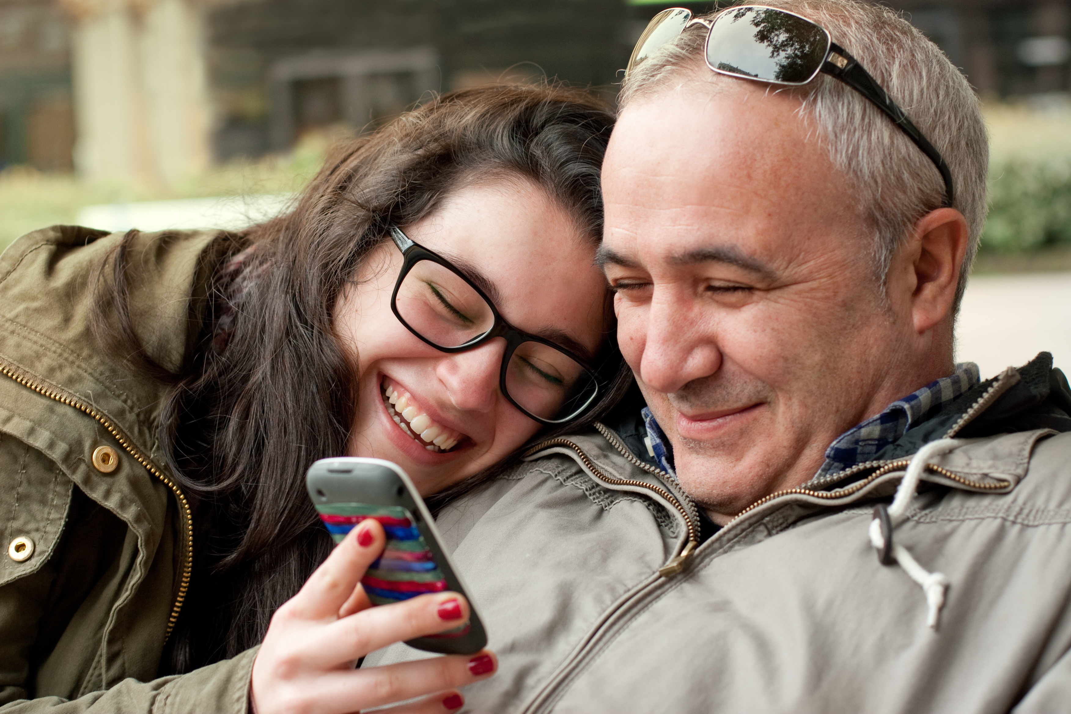 Ein Mann bindet sich an seine Tochter, während er auf ihr Telefon schaut | Quelle: Shutterstock