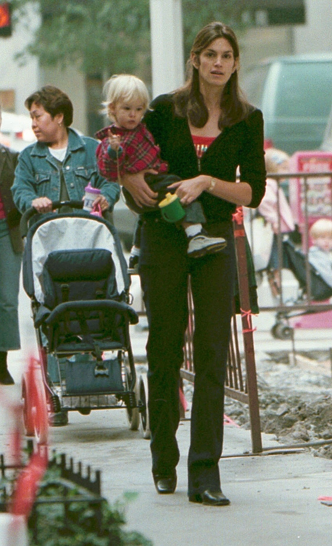 Cindy Crawford trägt am 27. Oktober 2000 den kleinen Presley Gerber bei einem entspannten Stadtrundgang durch Midtown Manhattan. Mit seinen weißblonden Haaren, den winzigen Turnschuhen und dem Flanellhemd hält Presley einen grünen Trinkbecher fest, während Crawford selbstbewusst an seiner Seite entlanggeht – ein ungezwungener Einblick in die frühe Mutterschaft vor dem Hintergrund des geschäftigen New Yorker Lebens.