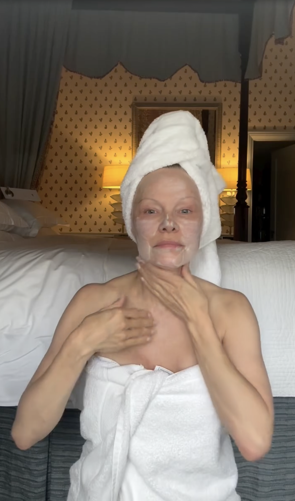Pamela Anderson cremt sich Hals und Dekolleté ein, während sie nach ihrer Morgenroutine in weiße Badetücher gehüllt ist und einen passenden Turban aus einem Handtuch trägt. Sie strahlt natürliche Selbstakzeptanz aus und feierte den Jahrestag ihrer ganzheitlichen Hautpflegeserie „Sonsie Skin“, indem sie das Video aus dem Schlafzimmer, in dem sie ungeschminkt zu sehen ist, mit einer nachdenklichen Reflexion verband: „Guten Morgen, Welt… 🤍 Heute ist ein Segen – denn wir feiern einen weiteren Geburtstag von @sonsieskin. Das Universum erfüllt Wünsche … was sind deine? Meiner ist es, noch dankbarer, verspielter … und weiser zu sein. ✨ Liebe, P“. | Quelle: Instagram/pamelaanderson