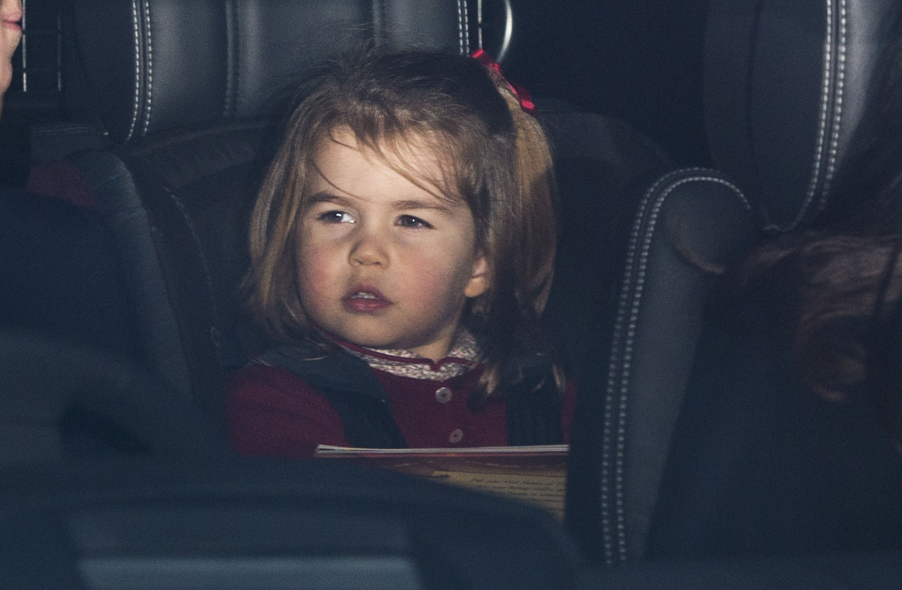 Prinzessin Charlotte von Cambridge schaut vom Rücksitz eines Autos hervor, das am 20. Dezember 2017 in London, England, zum jährlichen Weihnachtsessen der erweiterten königlichen Familie im Buckingham Palace vorfährt. Die kleine Prinzessin trägt eine festliche burgunderrote Strickjacke über einem gemusterten Oberteil mit Kragen, und ihr Haar ist mit einer passenden roten Schleife verziert. | Quelle: Getty Images