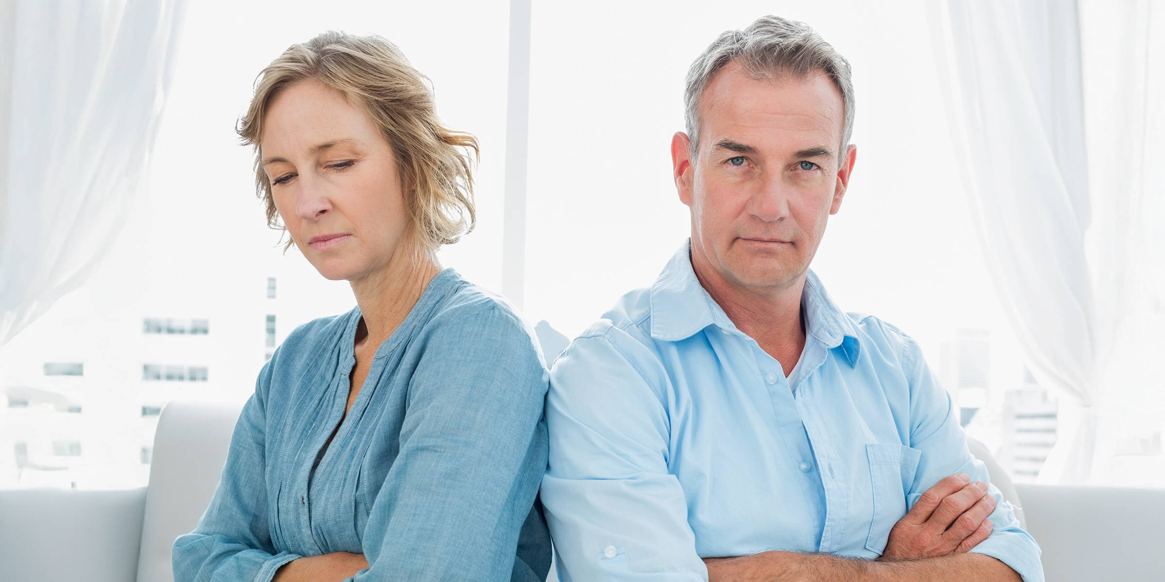 Ein angespanntes Paar mittleren Alters sitzt mit verschränkten Armen | Quelle: Shutterstock