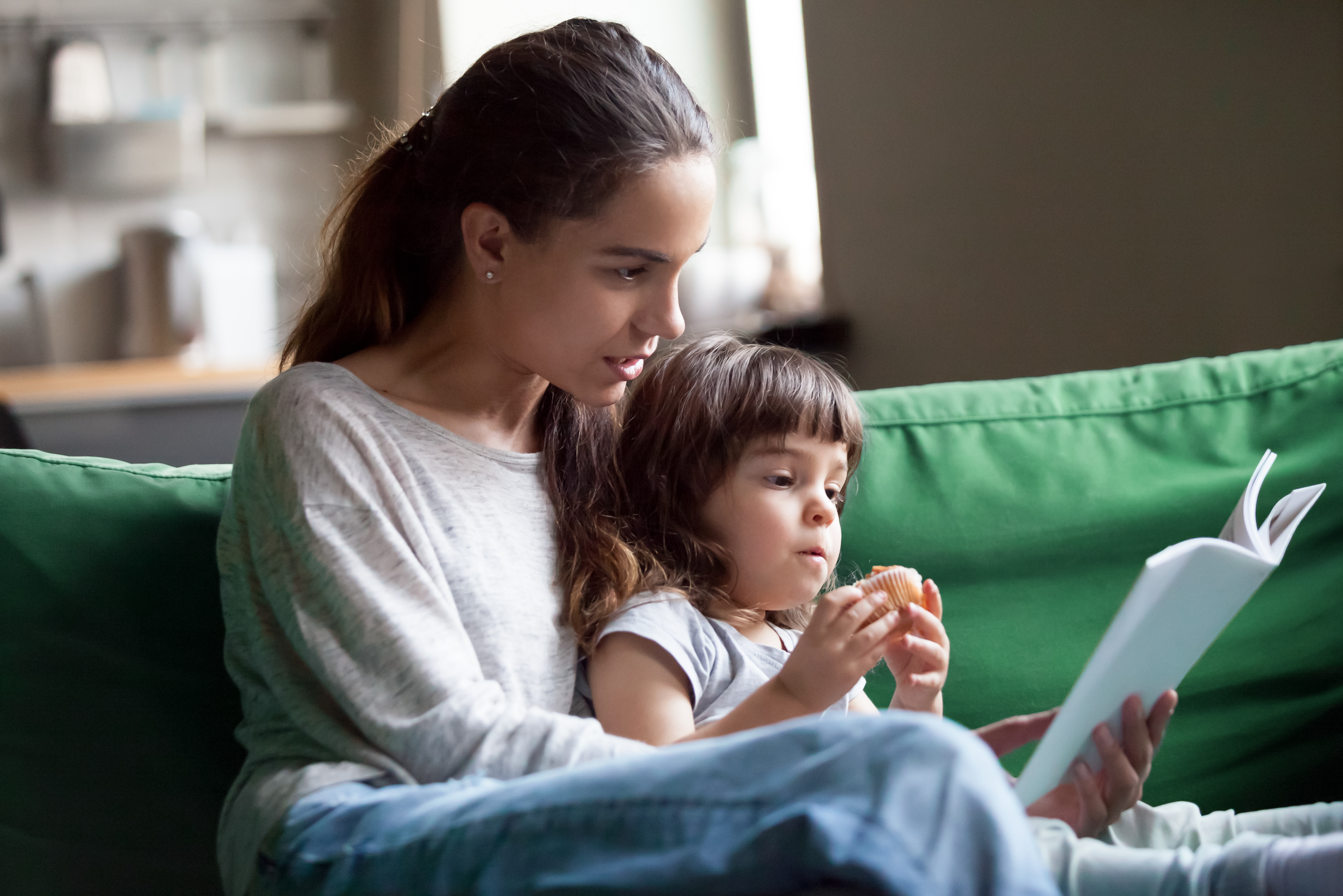 Eine junge Mutter liest ein Buch mit ihrem kleinen Mädchen | Quelle: Shutterstock