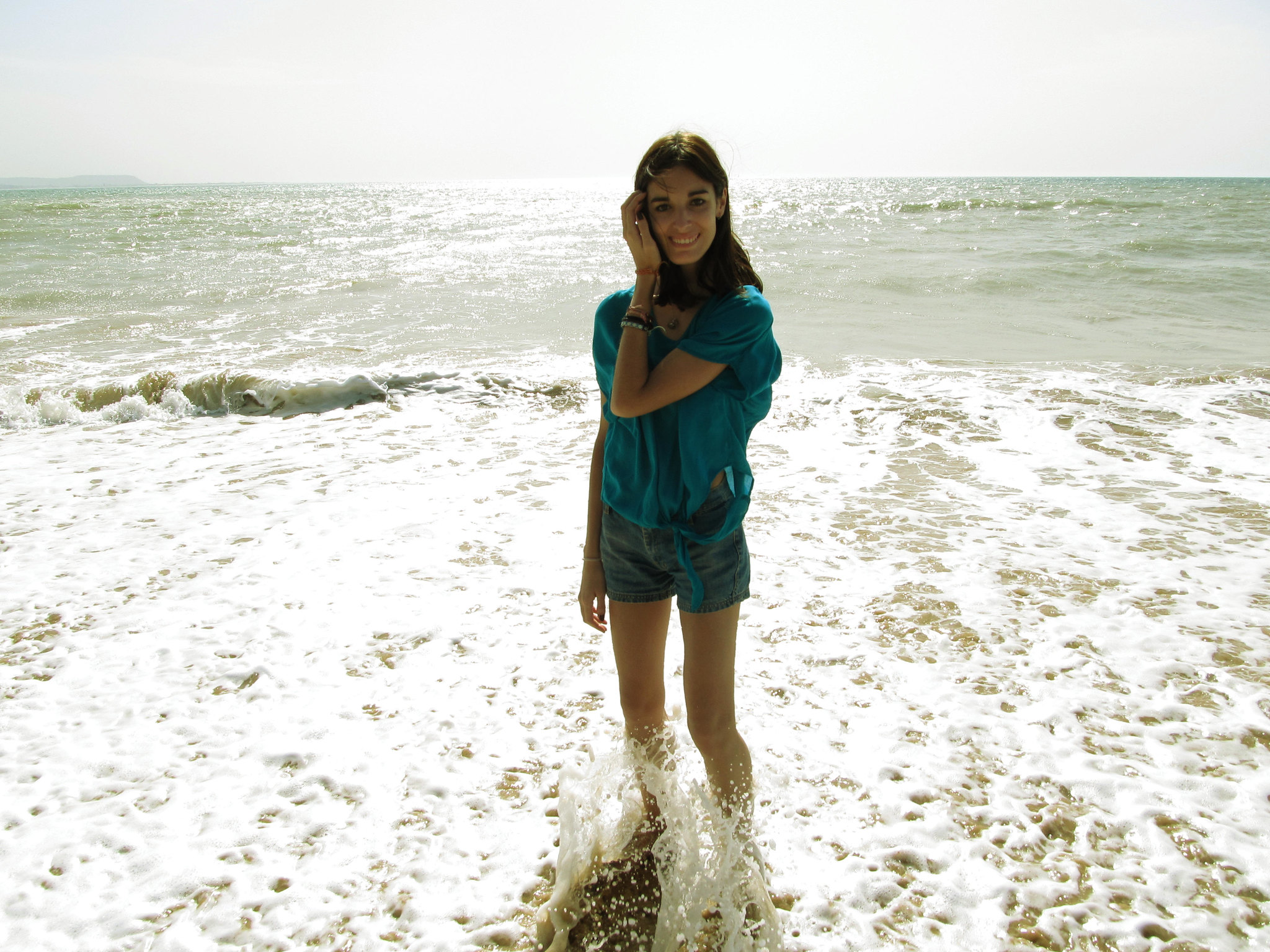 Eine junge Frau lächelt, während sie an einem Strand im Wasser steht | Quelle: Flickr