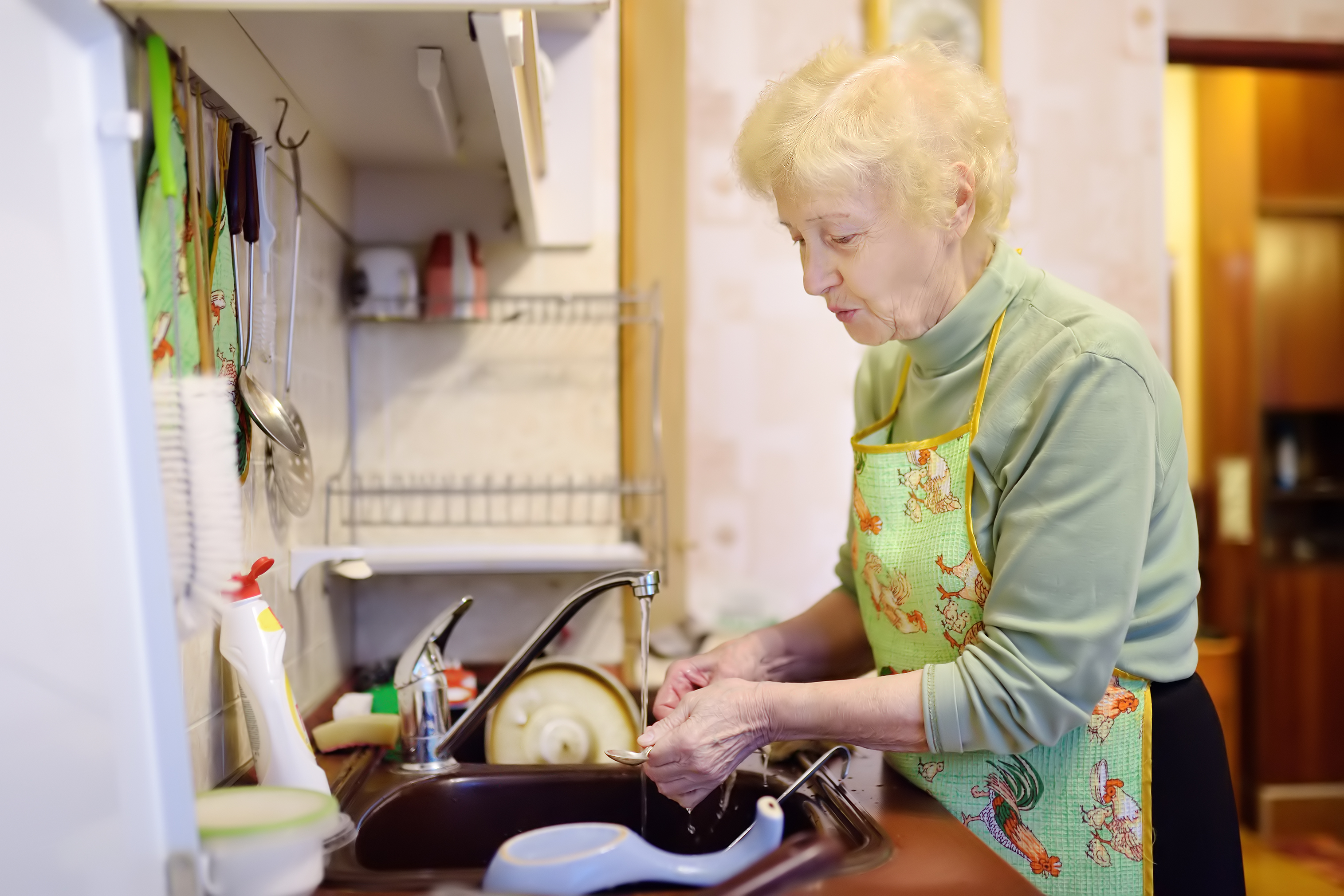 Eine ältere Dame wäscht in der Küche ab | Quelle: Shutterstock