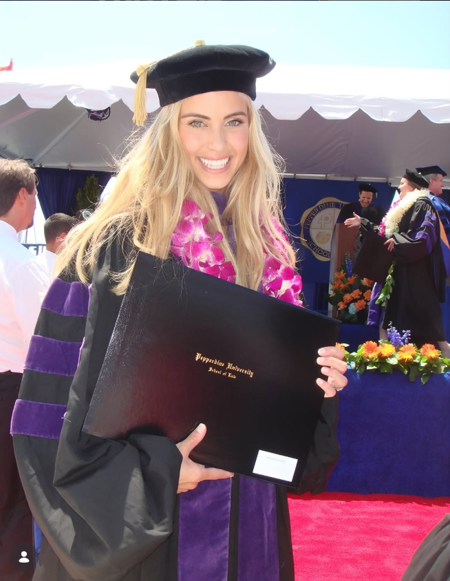 Katie Zacharia feiert ihren Abschluss an der Pepperdine Caruso School of Law in einem schwarzen akademischen Talar, einer mit violetten Borten verzierten Tracht und einem Doktorhut, während sie ihre Diplommappe in der Hand hält. Ihre Zeit an der Pepperdine legte den Grundstein für eine Karriere, die sie später von der Rechtswissenschaft zur politischen Kommunikation und ins Weiße Haus führen sollte. | Quelle: Instagram/katiezacharia