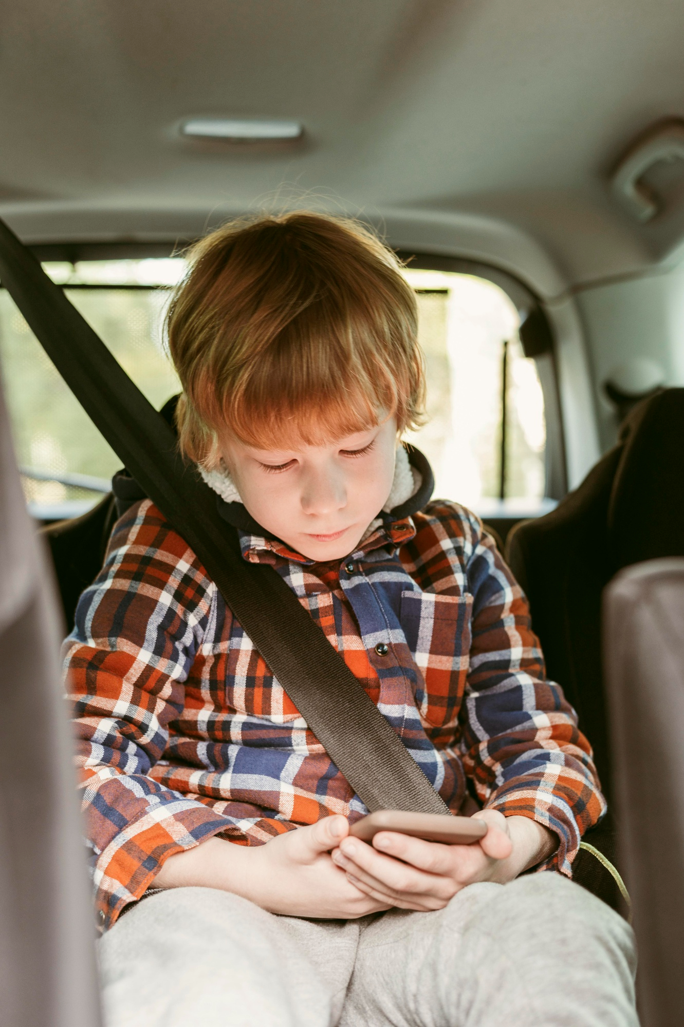 Ein kleiner Junge konzentriert sich auf ein Telefon auf dem Rücksitz eines Autos | Quelle: Freepik