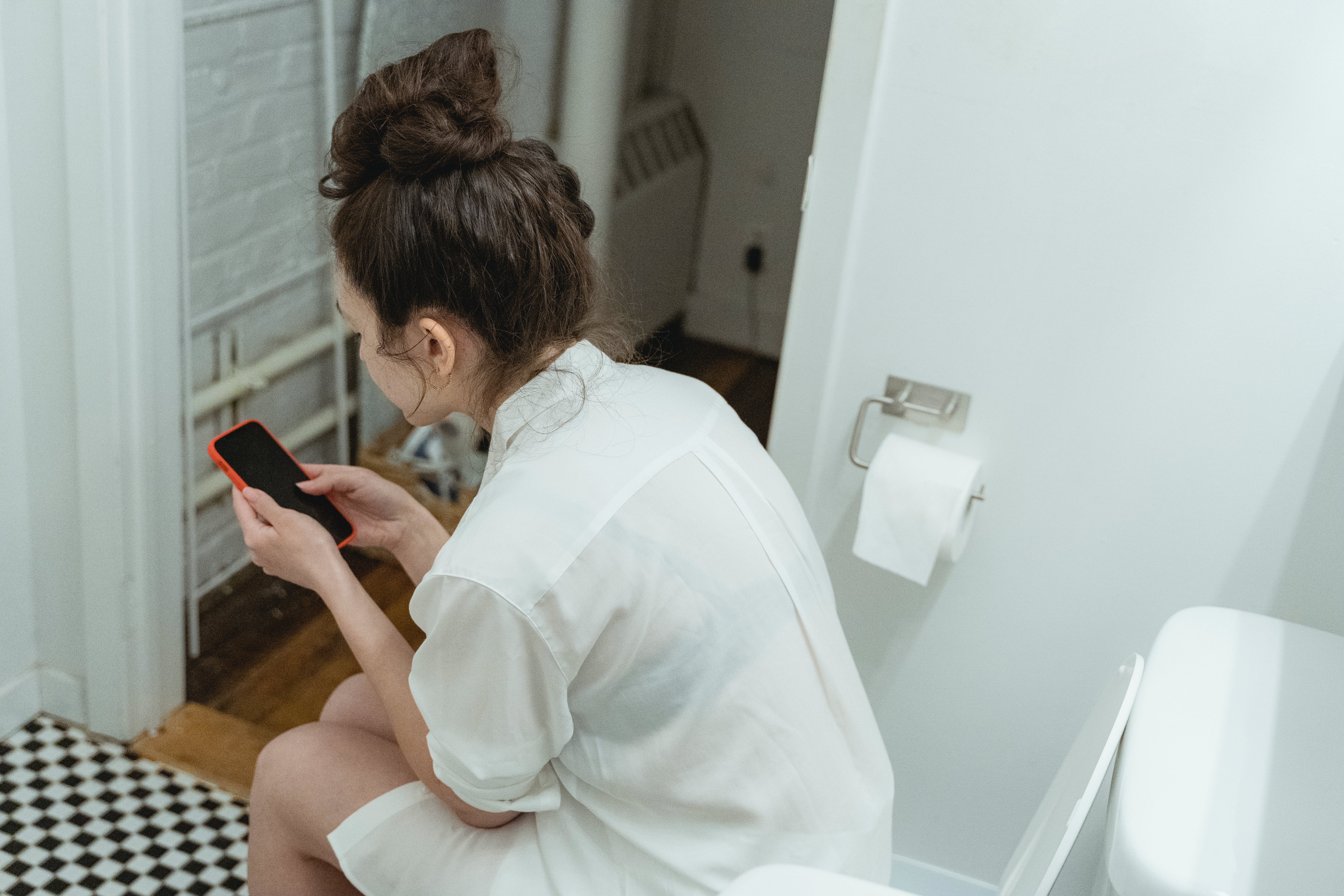 Eine Frau, die auf einer Toilette sitzt, während sie ihr Telefon benutzt | Quelle: Pexels