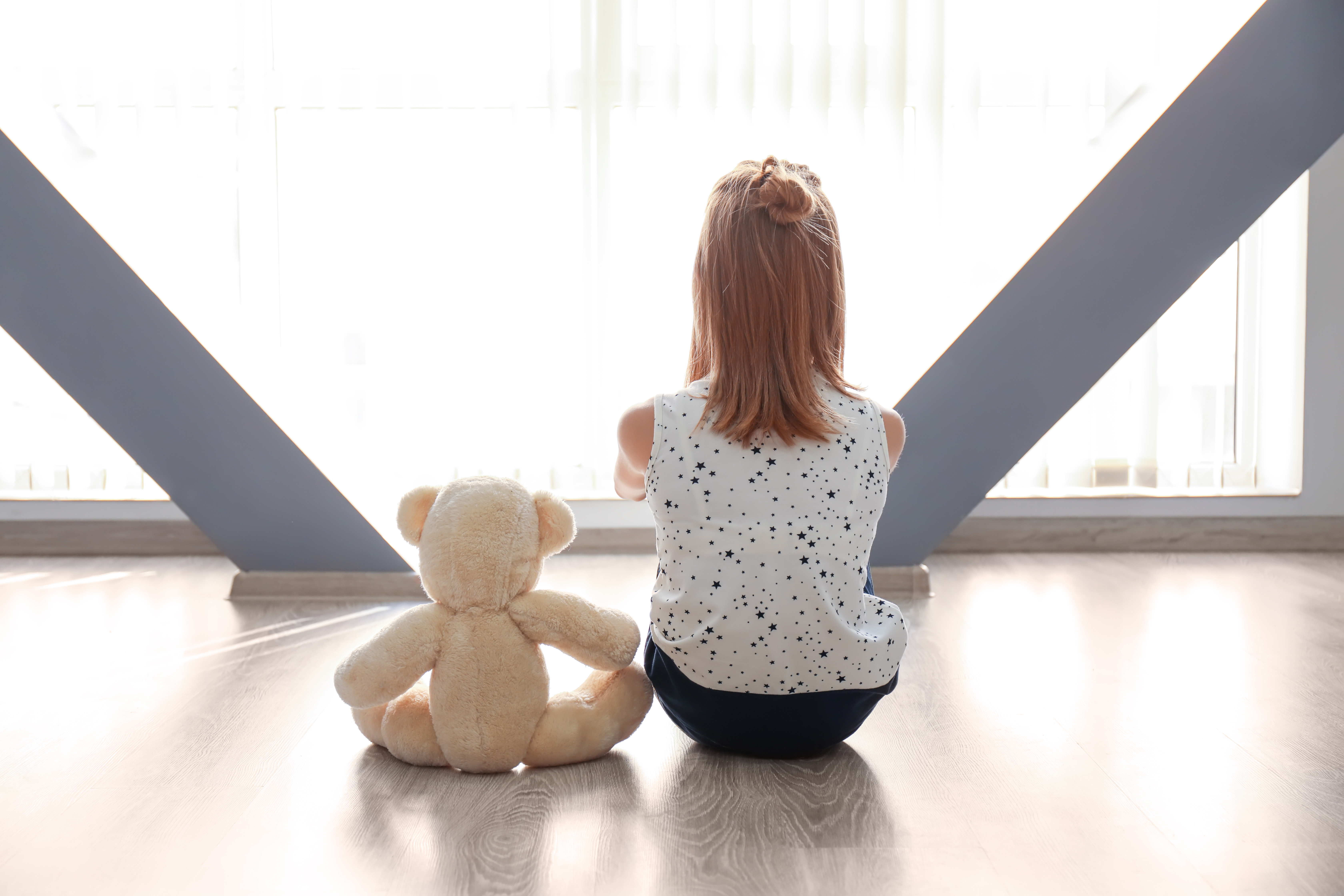 Ein kleines Mädchen sitzt mit ihrem Teddybär auf dem Boden | Quelle: Shutterstock