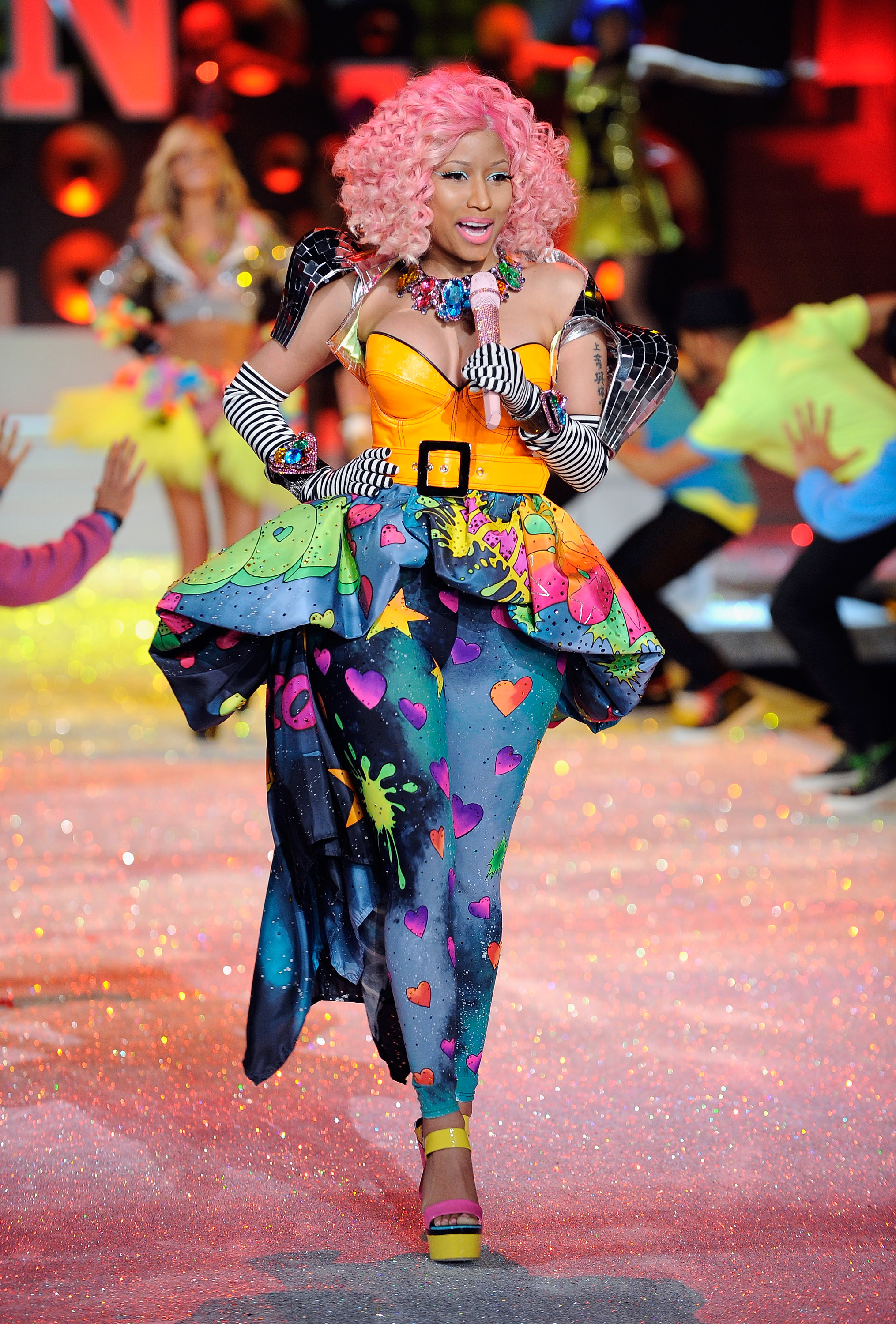 Nicki Minaj performt ihren Hit „Super Bass“ bei der Victoria’s Secret Fashion Show 2011 in New York – in einem leuchtend orangefarbenen Korsett, einem bunten Outfit mit Herzmuster und einer lockigen rosa Perücke. Ihr Auftritt war Teil des „Club Pink“-Segments der Show. | Quelle: Getty Images
